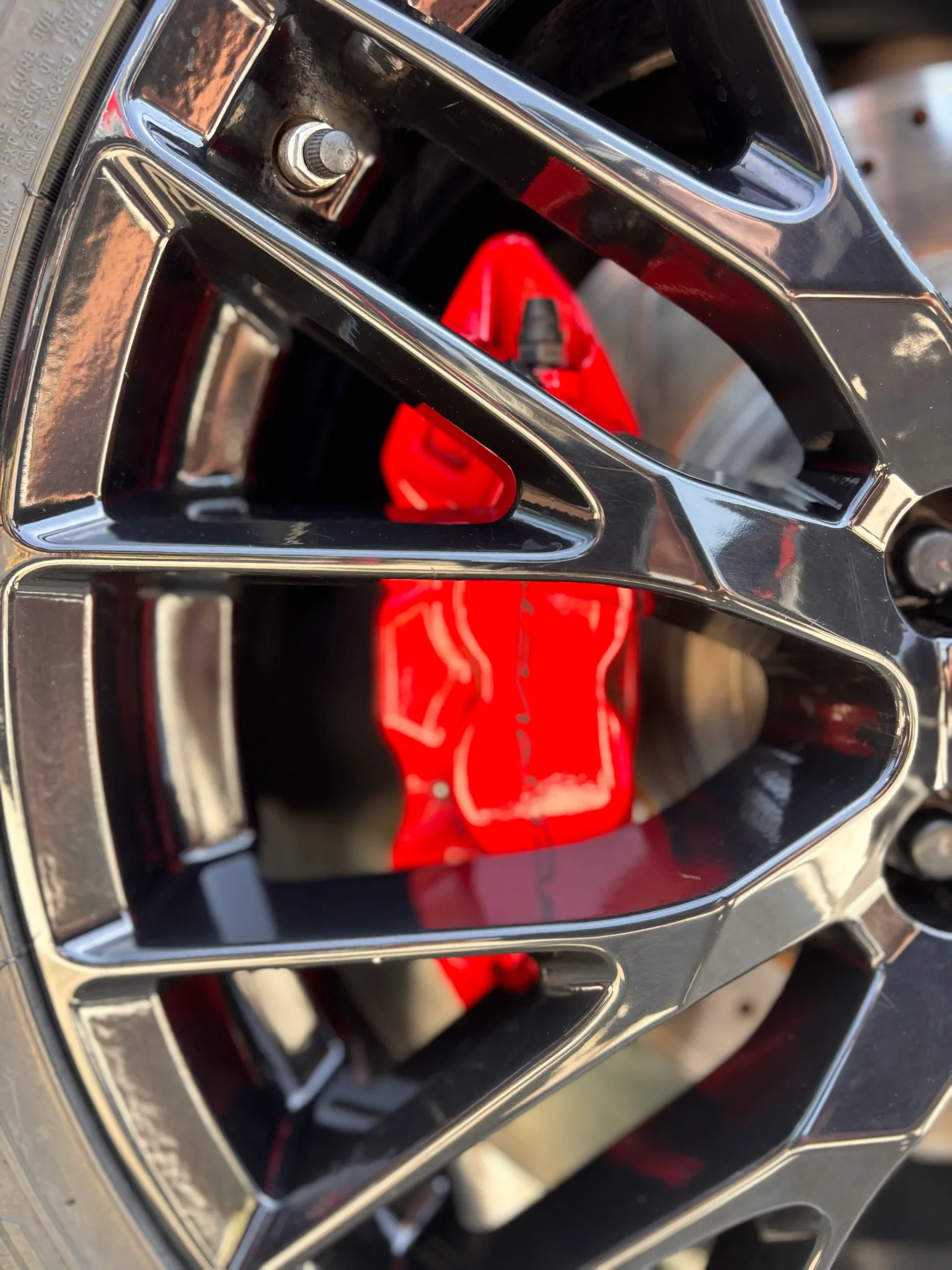 Macro of a red brake caliper seen through the spokes of a Corvette alloy wheel.