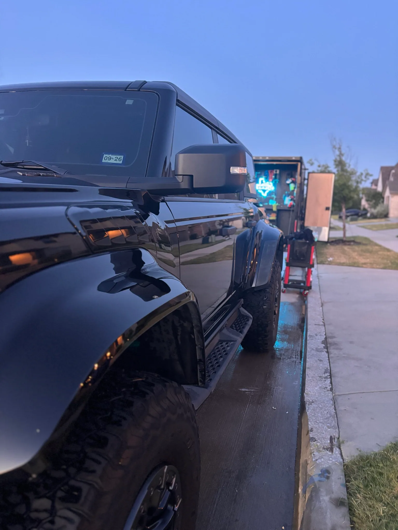 Close-up of the glossy fender and hood of a black Ford Bronco Raptor at dusk.
