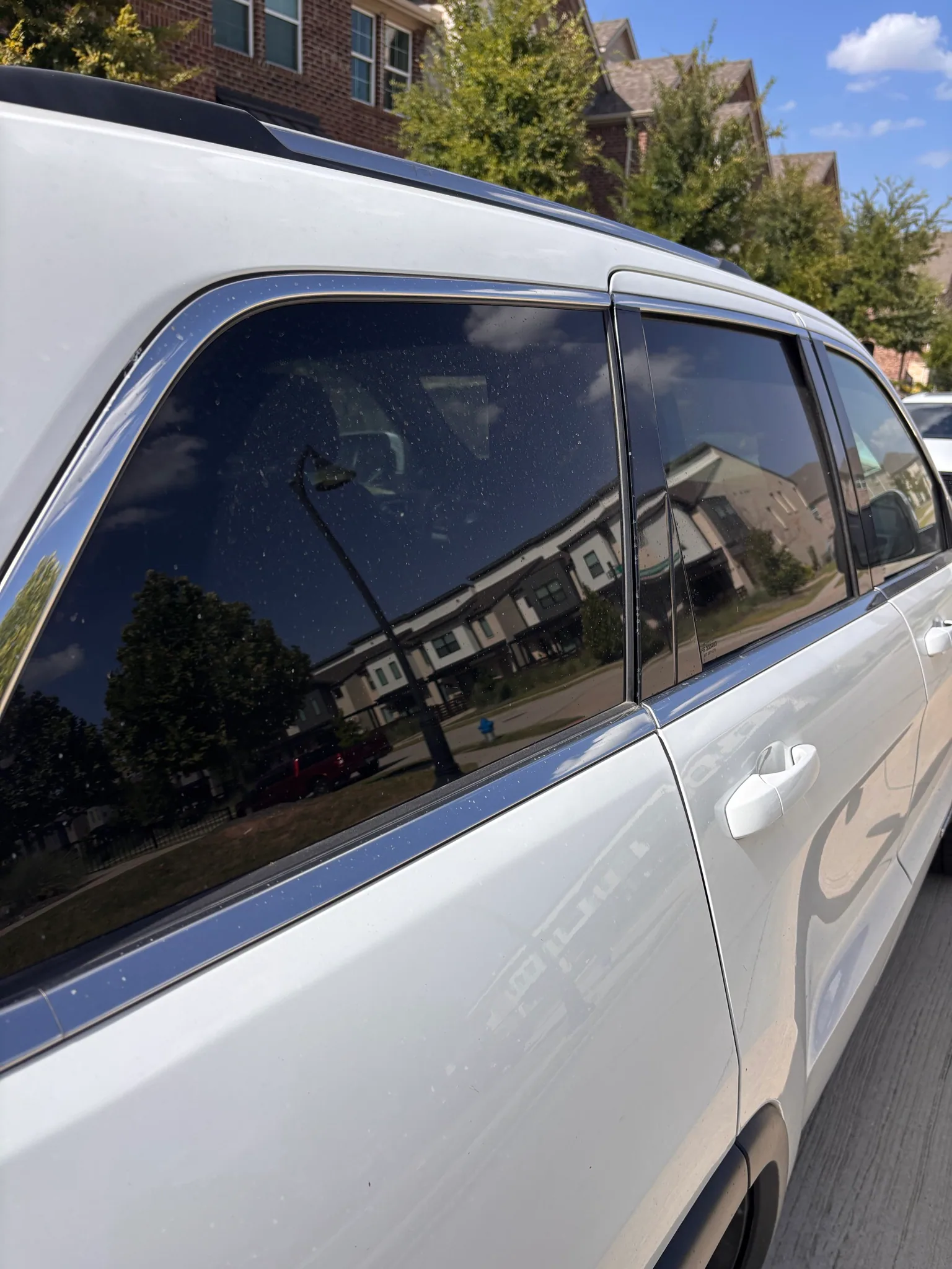 Clean side glass and doors of a white Jeep Grand Cherokee reflecting the street.
