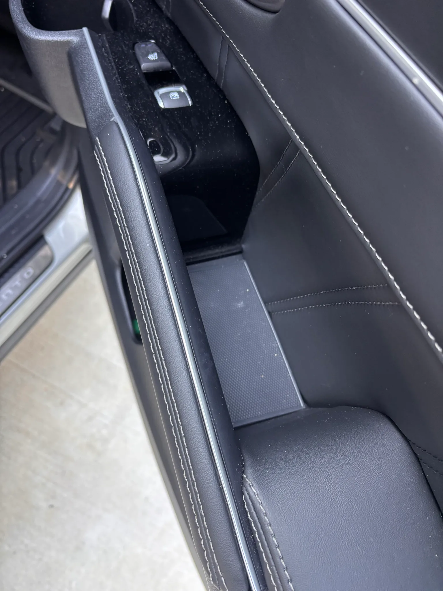 Close-up of the dusty door trim, window switches and leather seat edge inside a Kia Sorento.