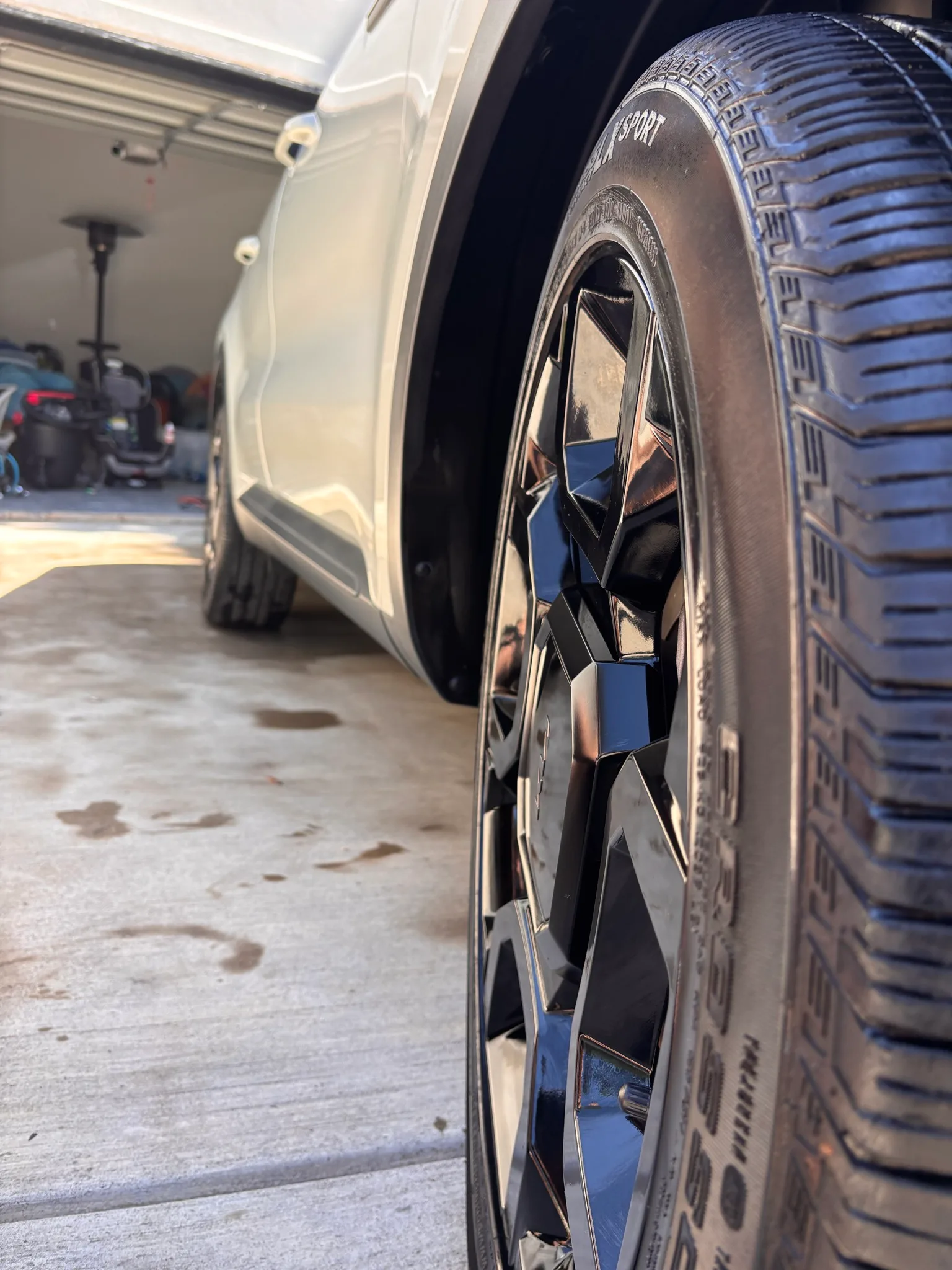 Low close-up of a gloss black alloy wheel and freshly dressed tire on a white Kia Sorento.