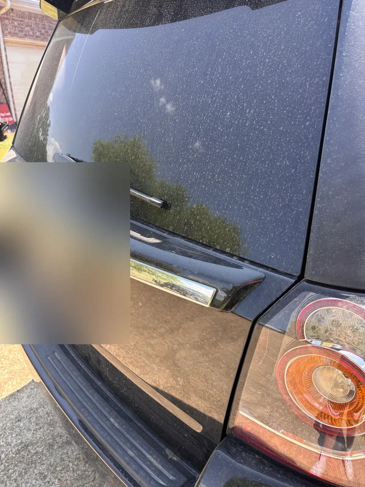 Close-up of hard water spots covering the rear glass and tailgate of a black Land Rover LR2.