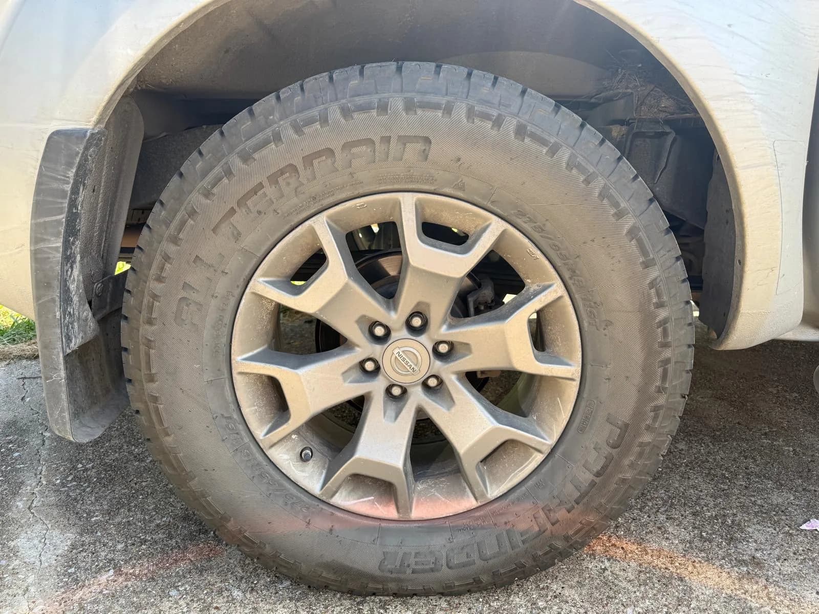 Close-up of a Nissan alloy wheel with an all-terrain tire before cleaning.