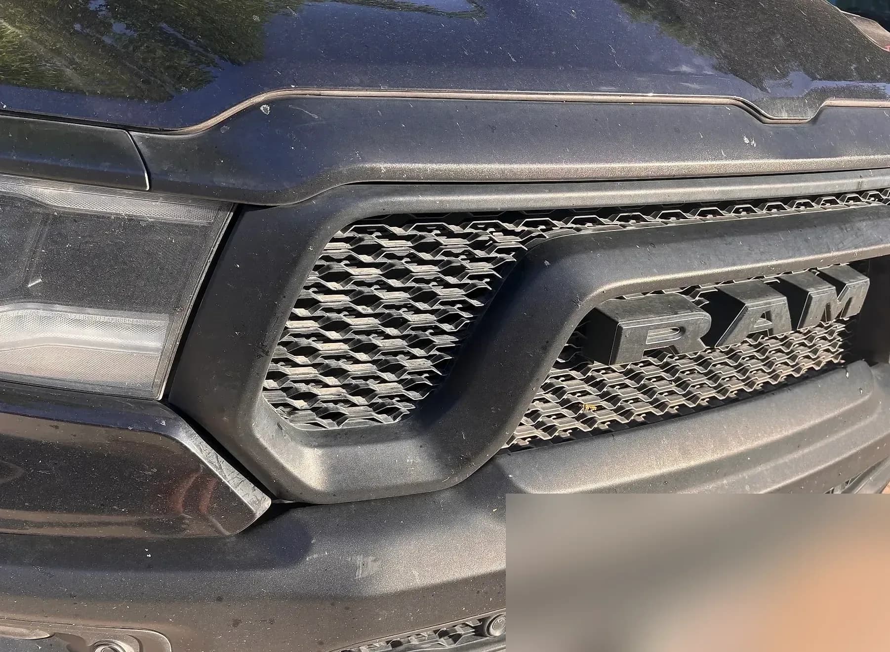 Front grille and RAM badge of a black Ram 1500 in detail.