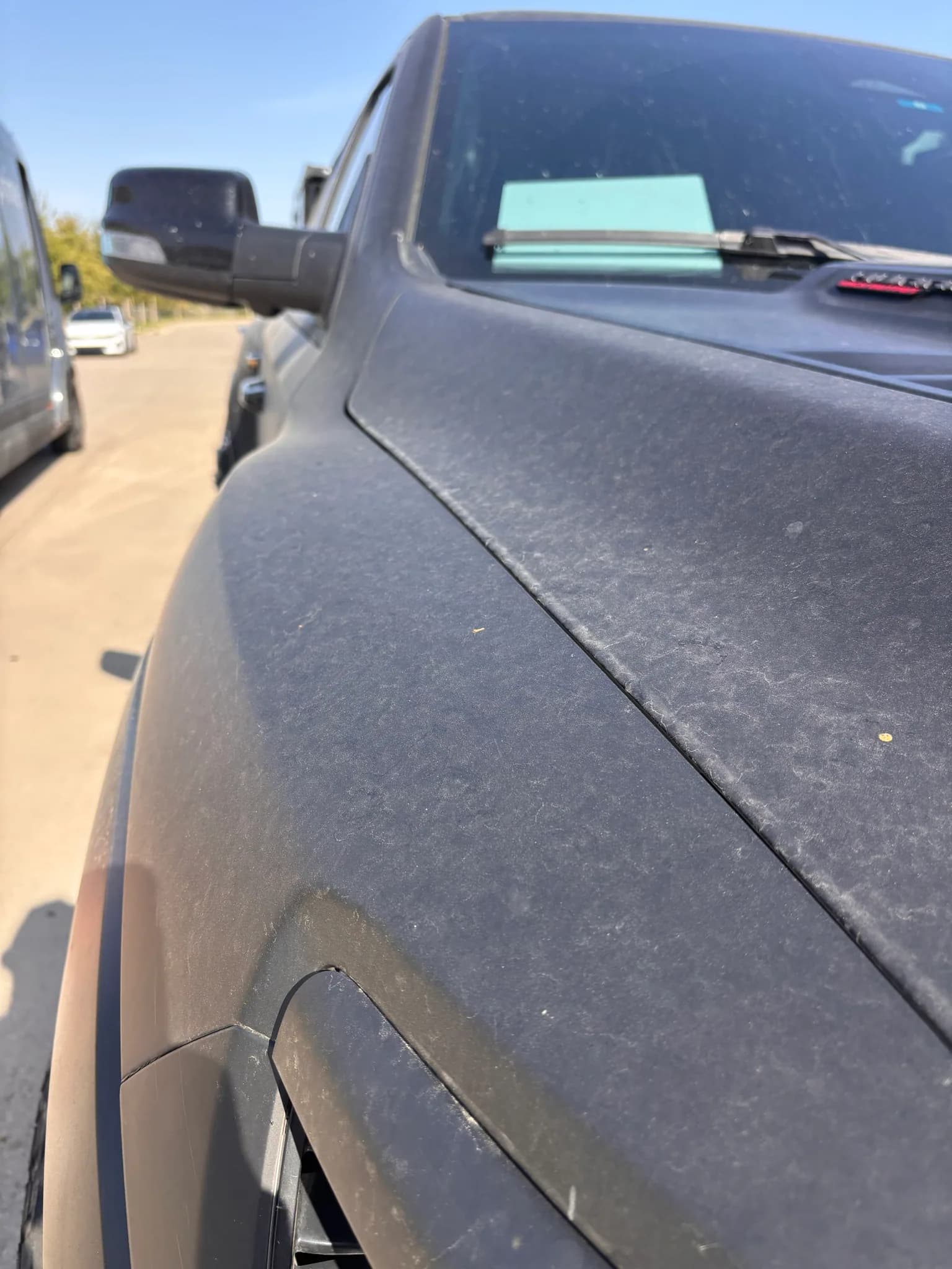 Close-up of the hood and windshield cowl of a matte grey Ram 1500 TRX, with road dust across the flat finish.