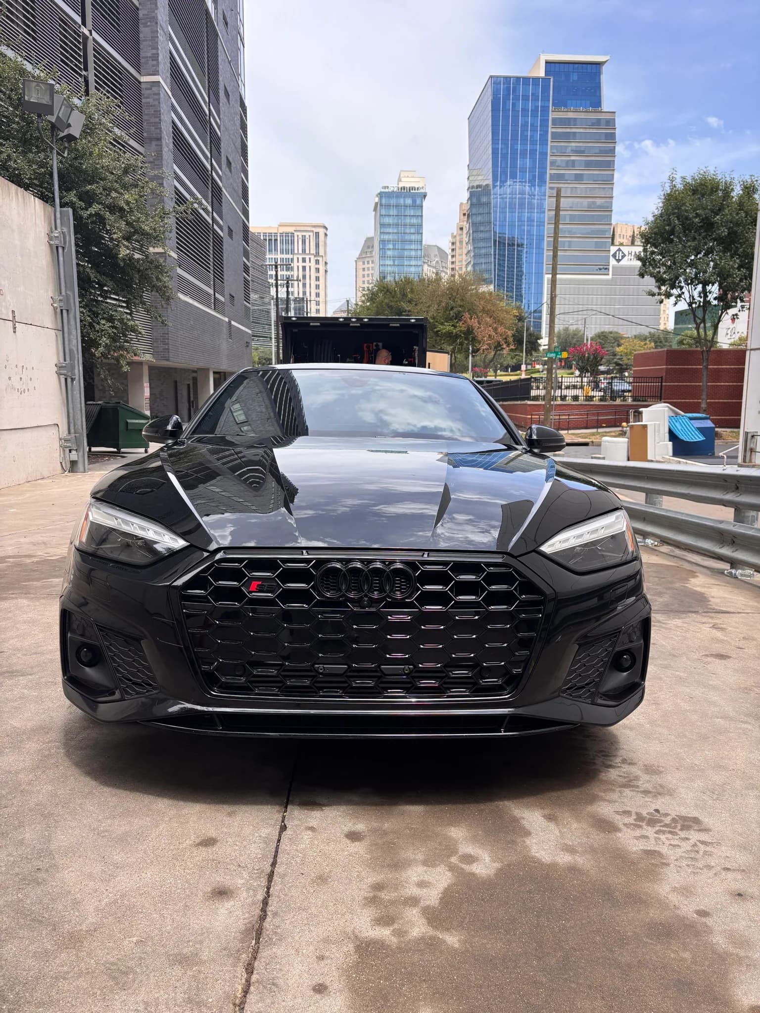 Straight-on front view of a black Audi S5 with the downtown skyline behind it.