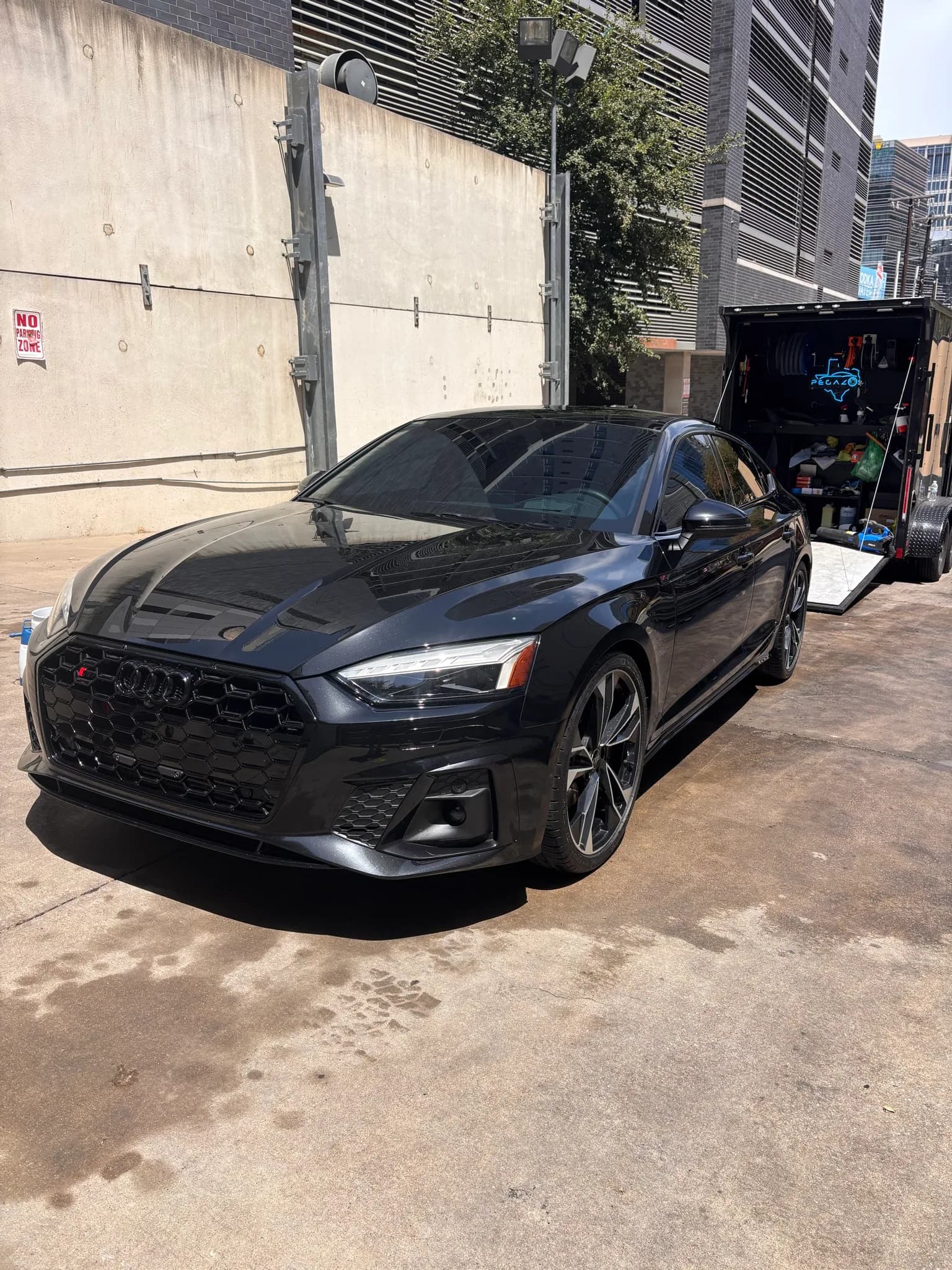 Front three-quarter view of a black Audi S5 beside the mobile detailing trailer.