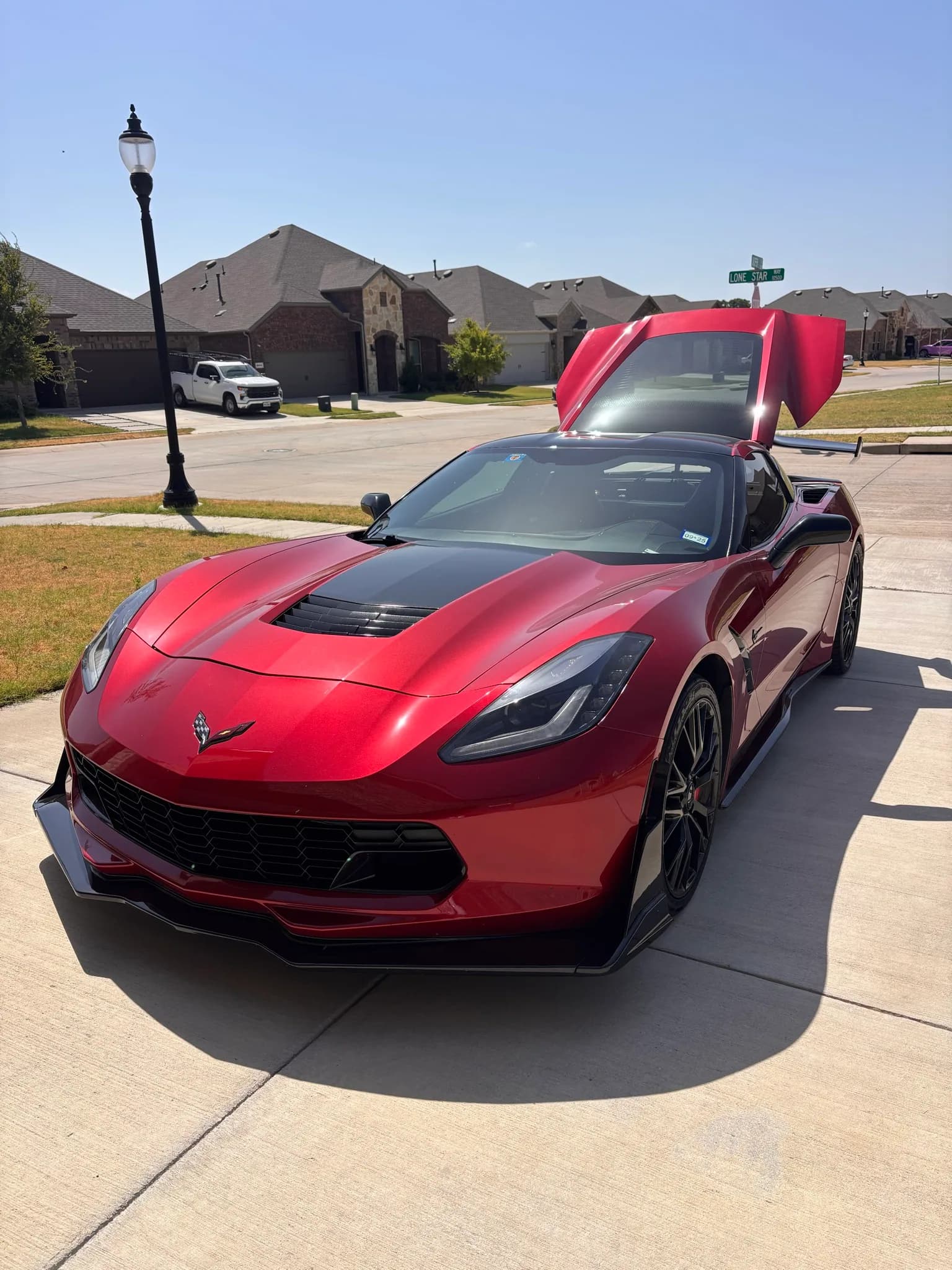 Red Chevrolet Corvette C7 with both doors open, front three-quarter view on a suburban street after detailing.