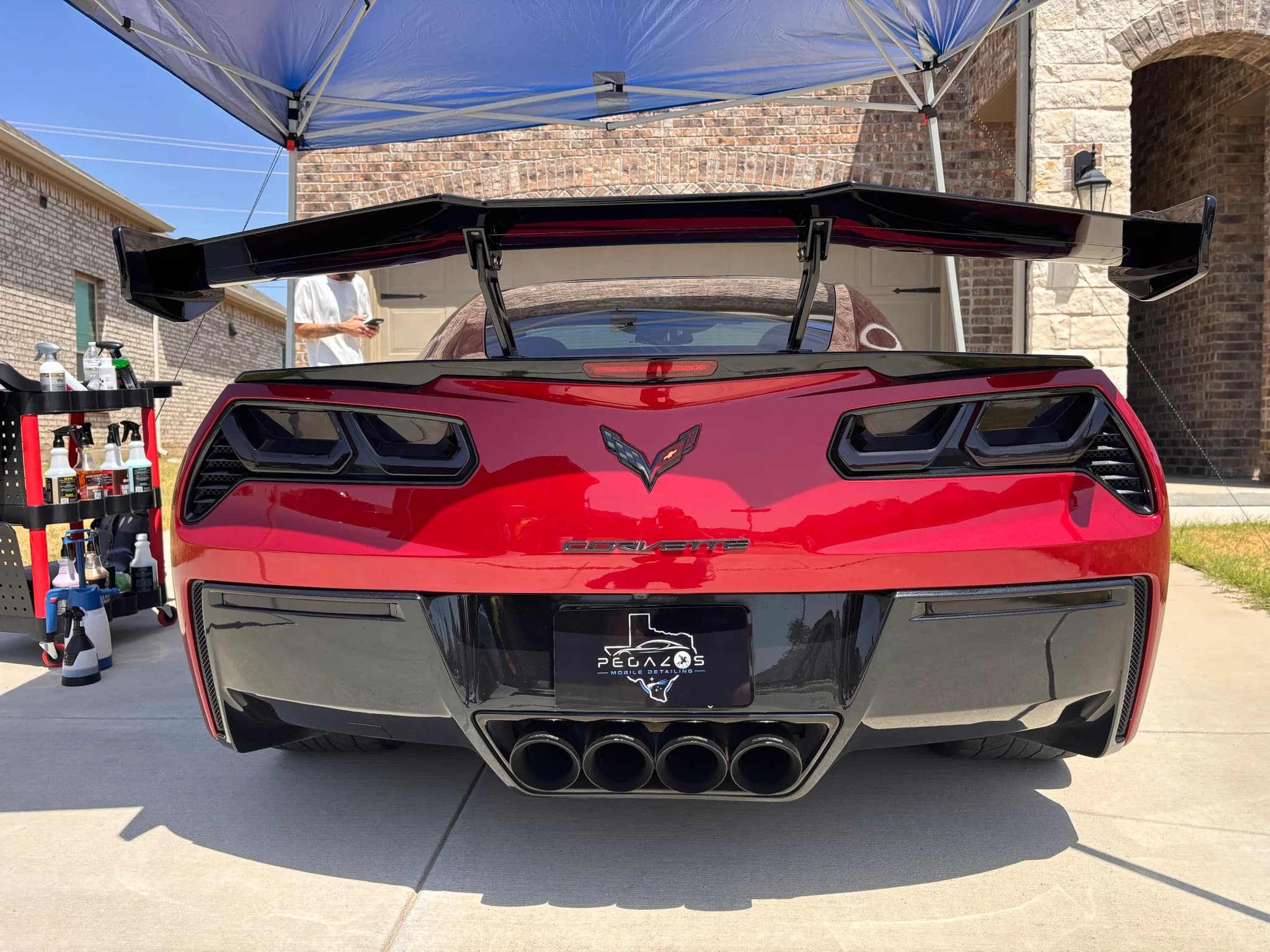 Straight-on rear view of a red Corvette under a work canopy, wing and diffuser cleaned.