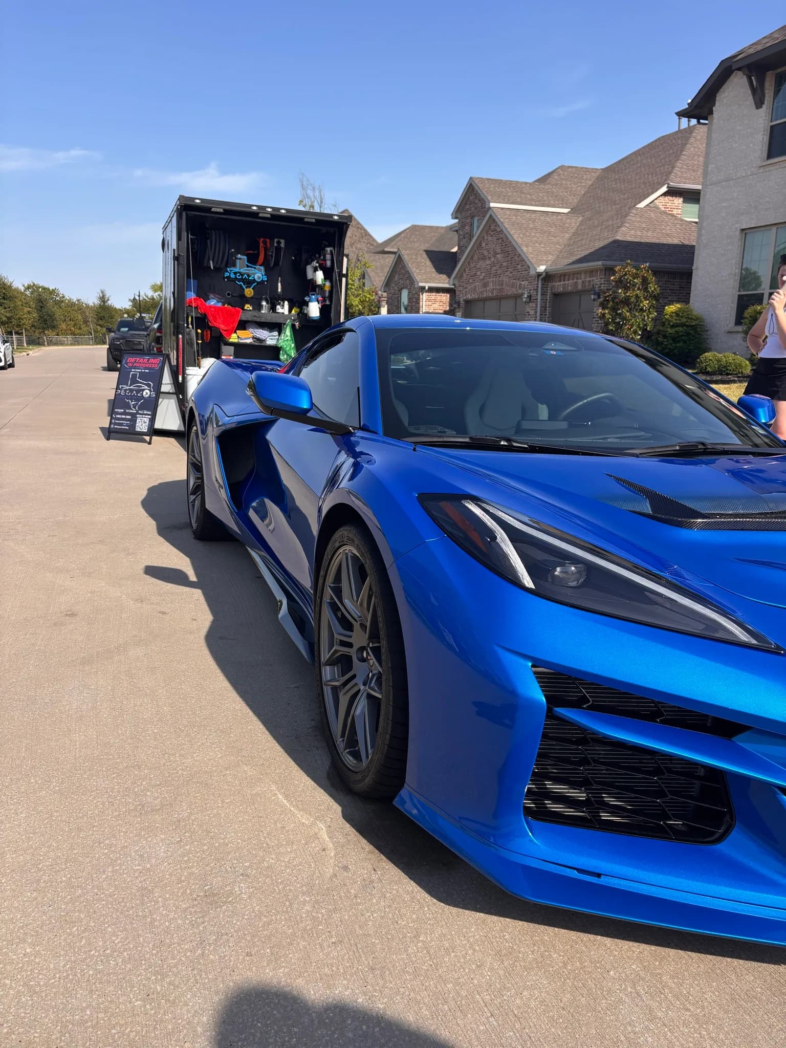 Front three-quarter view of a blue Corvette C8 Z06 beside the detailing trailer.
