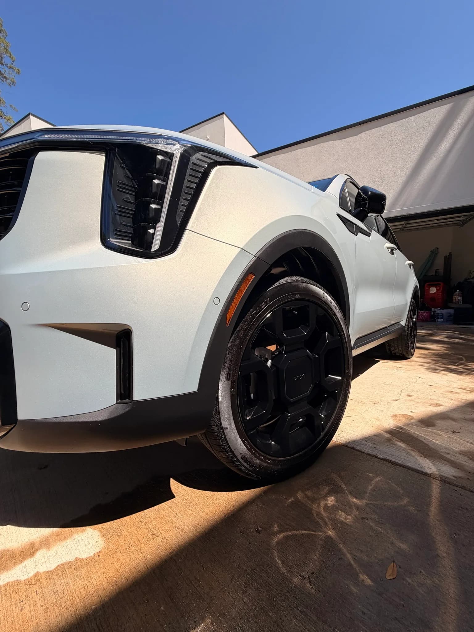 Low-angle front quarter view of a freshly detailed white Kia Sorento X-Line with gloss black wheels on a sunny driveway.