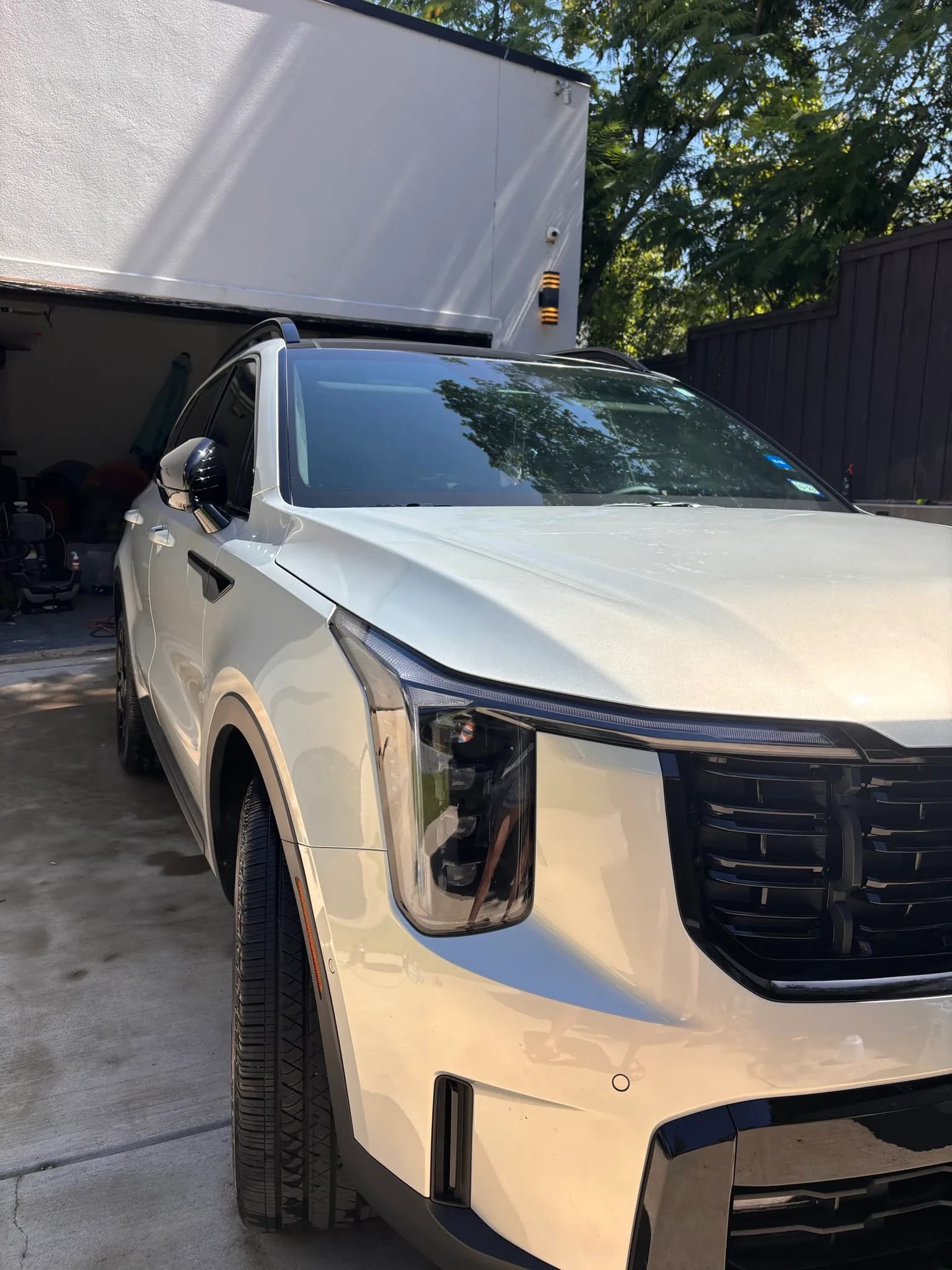 White Kia SUV with clean paint and headlights parked beside a work trailer.