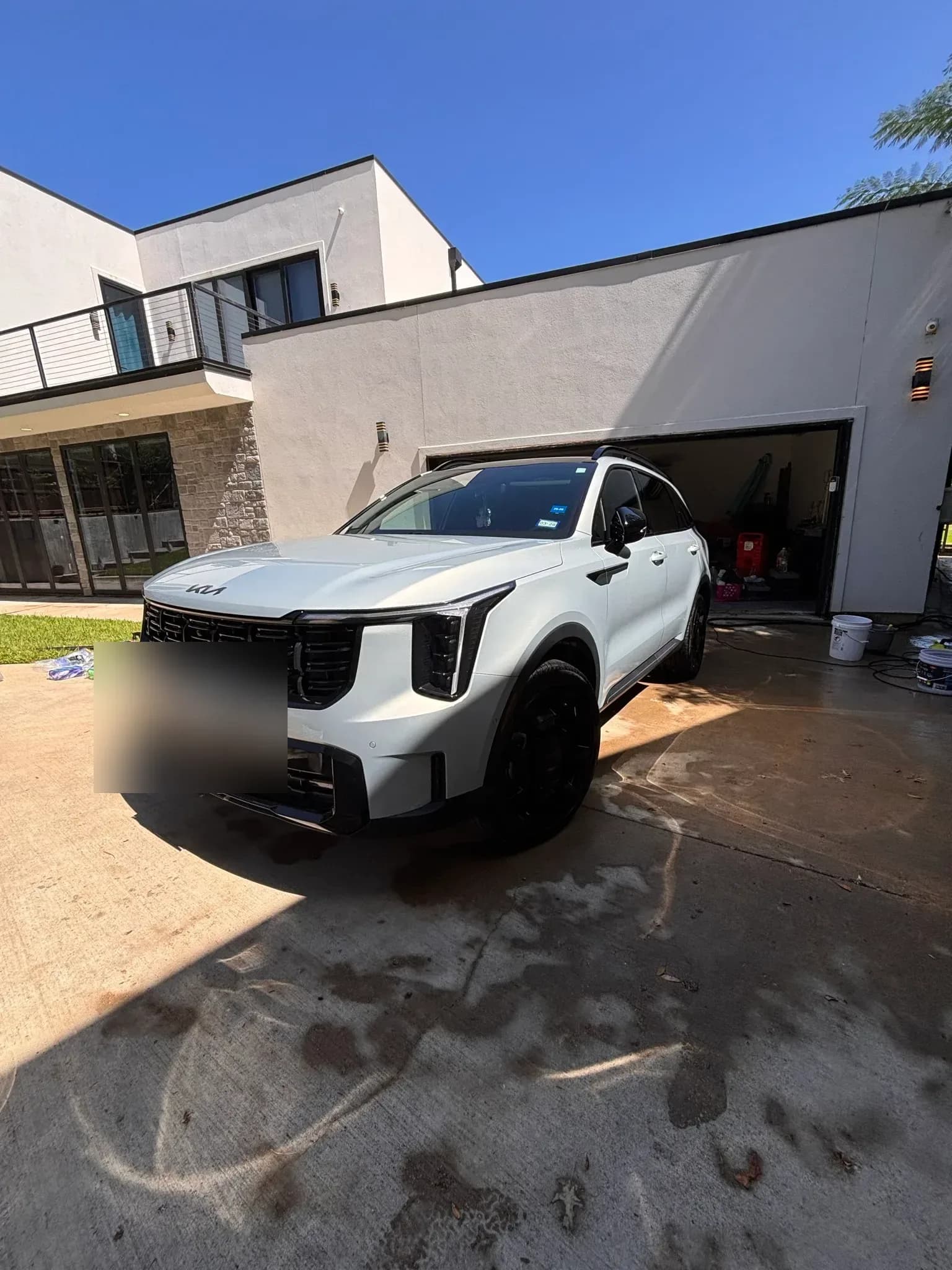 Wide shot of a freshly detailed white Kia Sorento on a driveway beside a modern home.