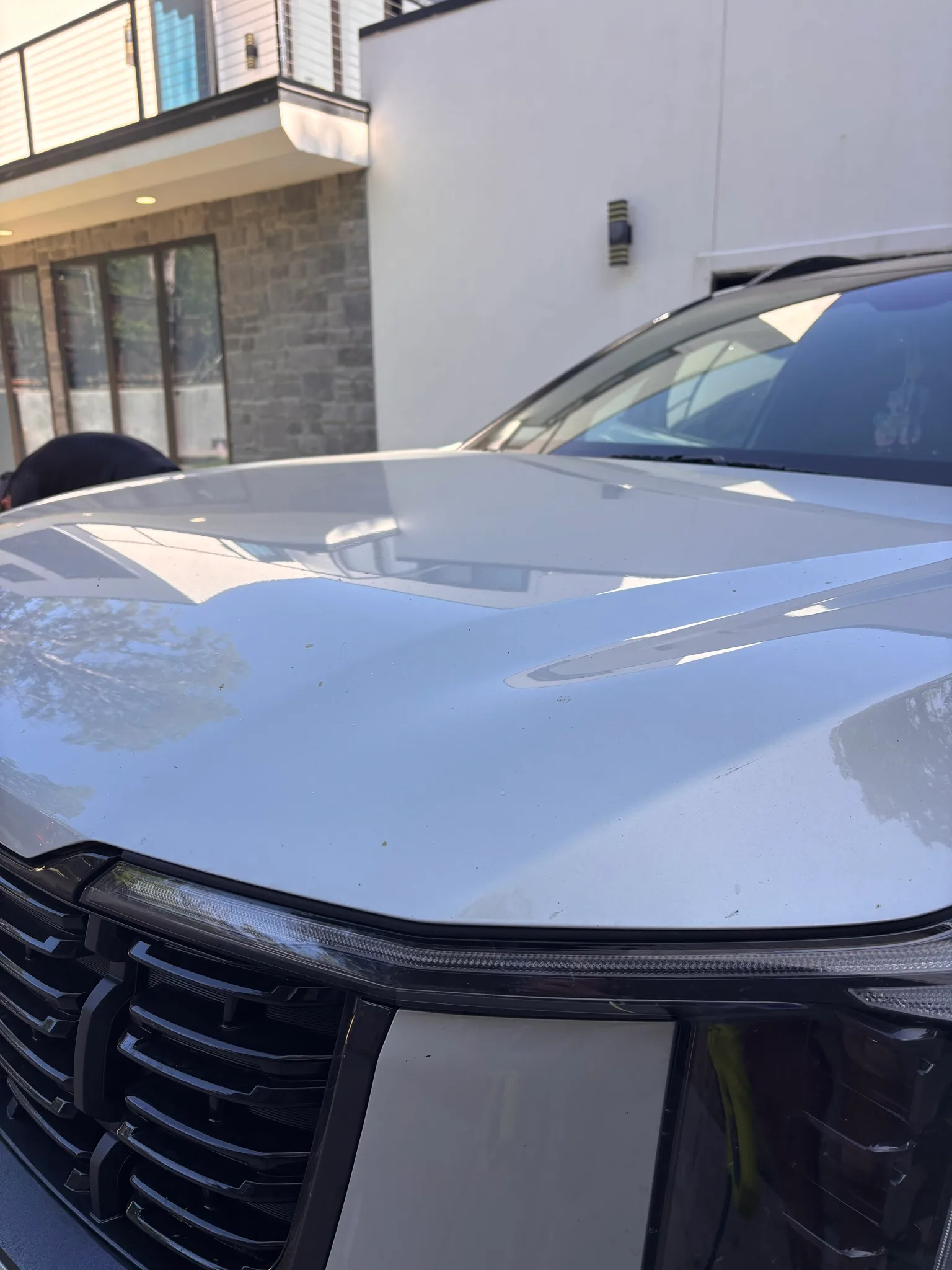 Clean, reflective hood and windshield of a white Kia SUV parked in front of a modern house.