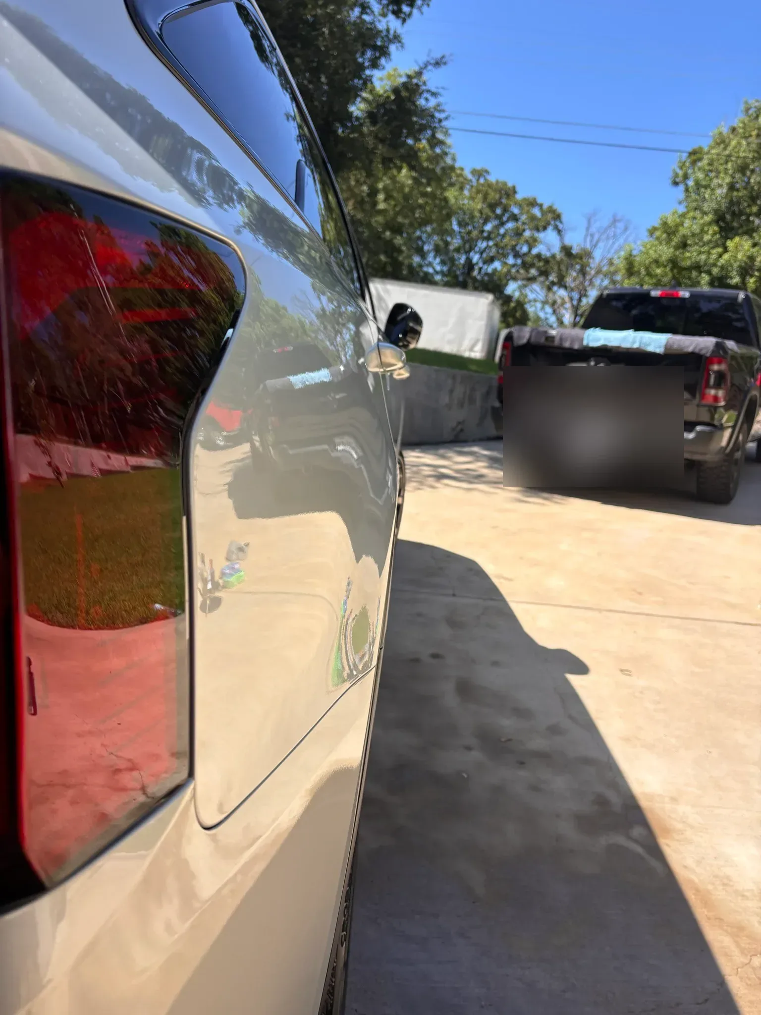 Mirror-like reflection on the rear panel of a detailed white SUV, with a black pickup truck in the background.