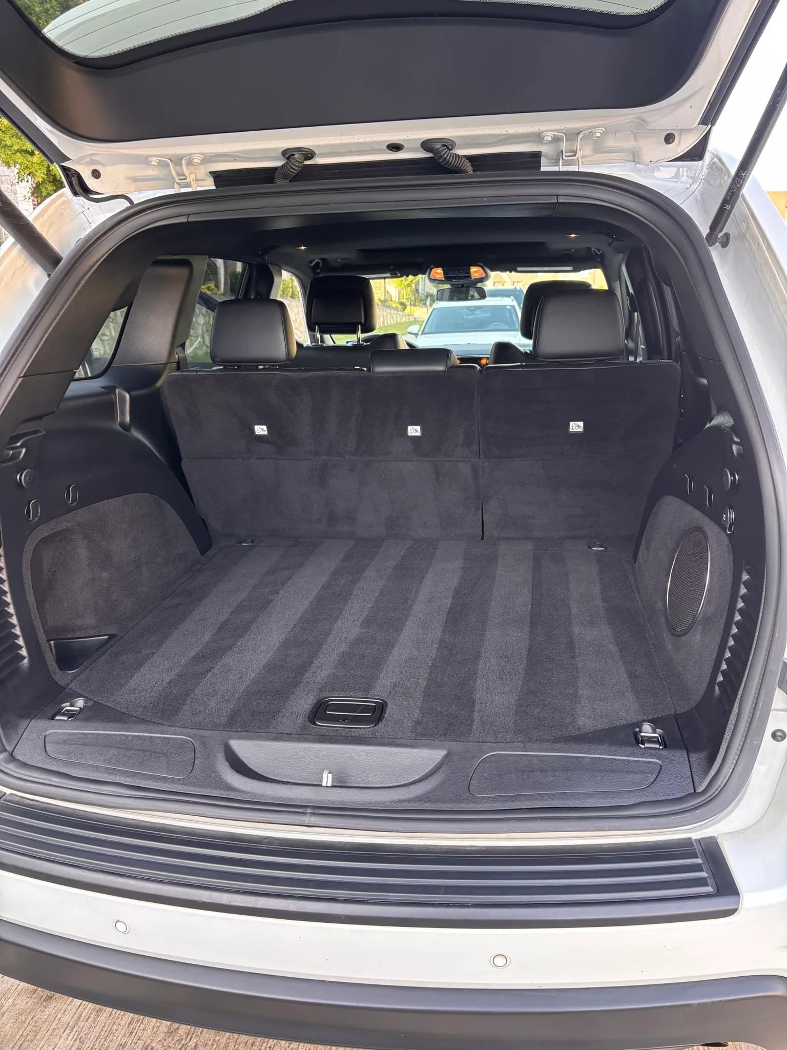 Open rear hatch and vacuumed cargo area of a white Jeep Grand Cherokee.
