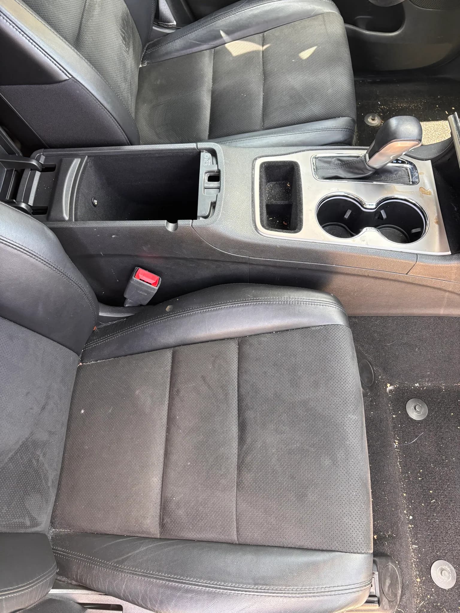 Front seats and center console inside a Jeep Grand Cherokee, with a dried spill on the console trim and crumbs in the tray before cleaning.