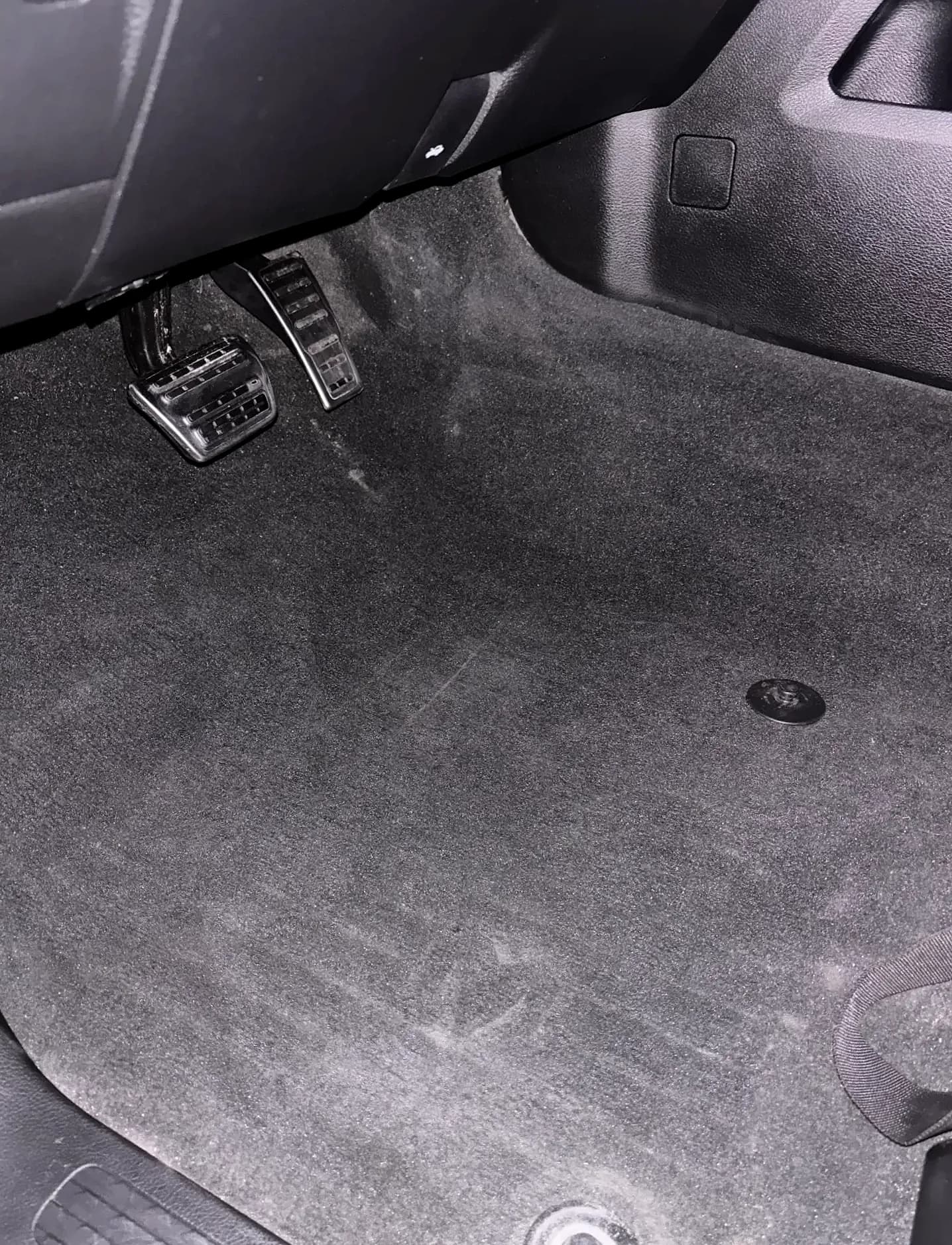 Driver footwell with clean carpet and alloy pedals.