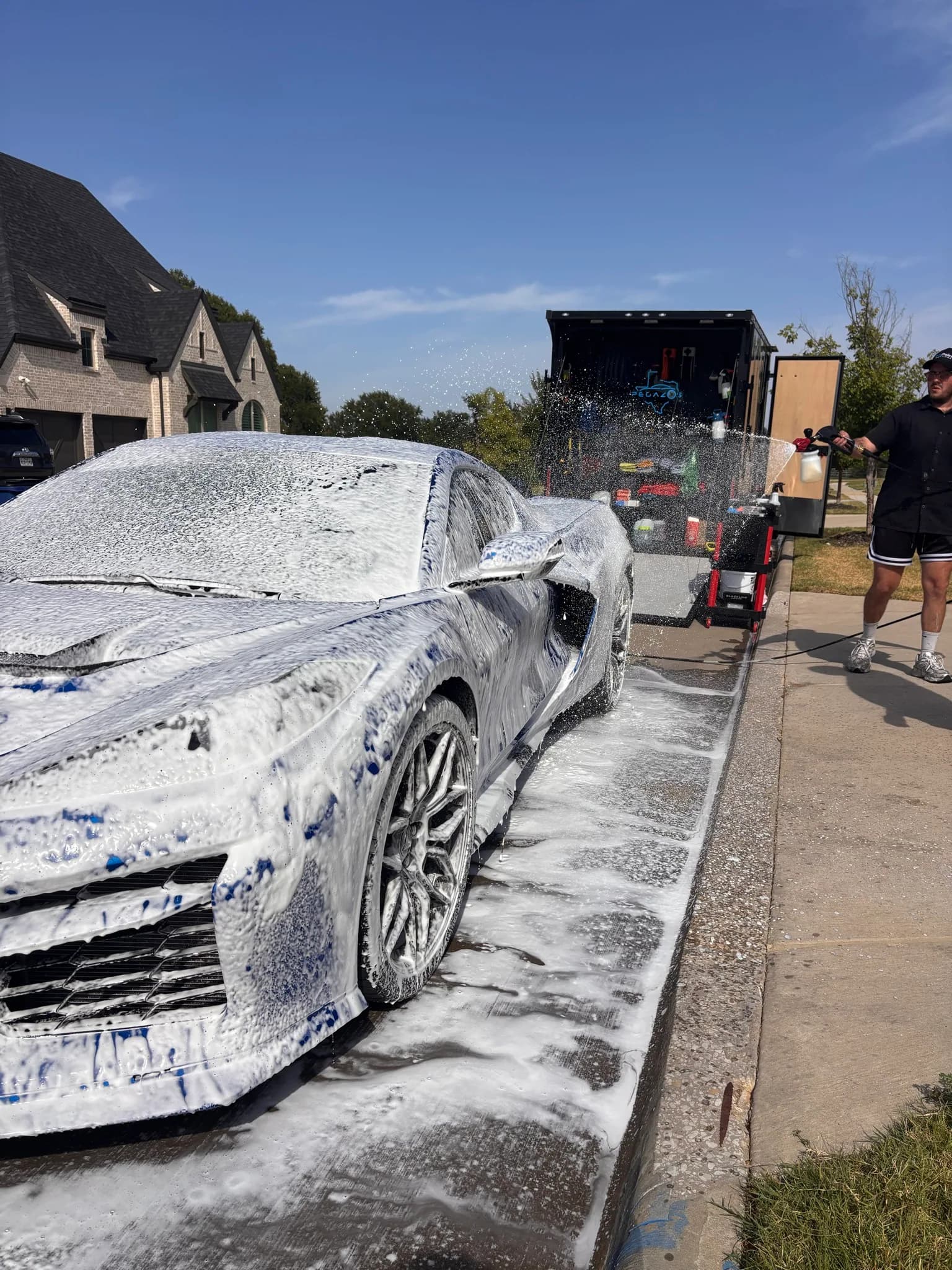 Corvette C8 Z06 under a full coat of wash foam with the detailer rinsing behind it.
