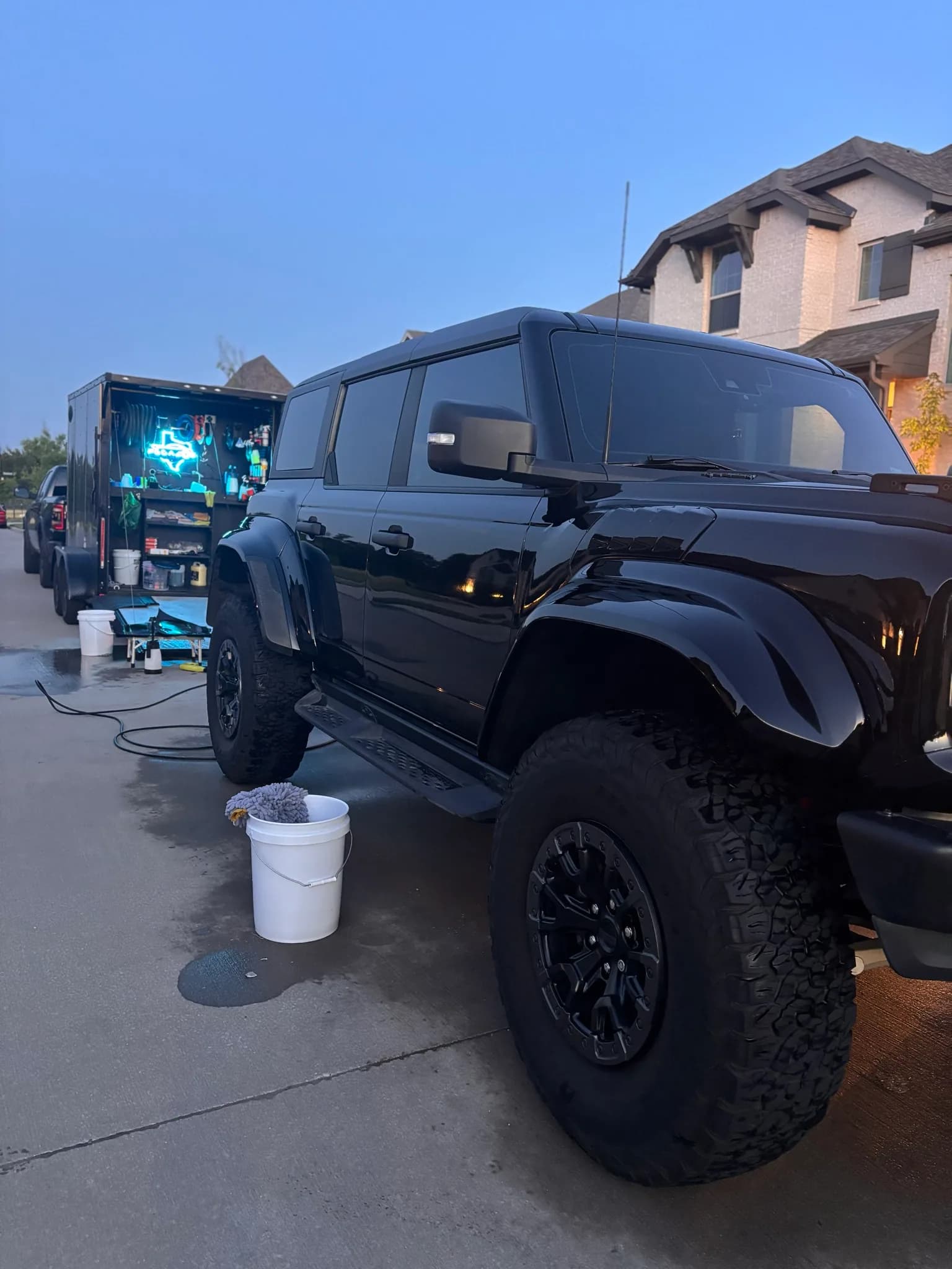 Black Ford Bronco Raptor mid-wash beside a wash bucket and the mobile trailer.