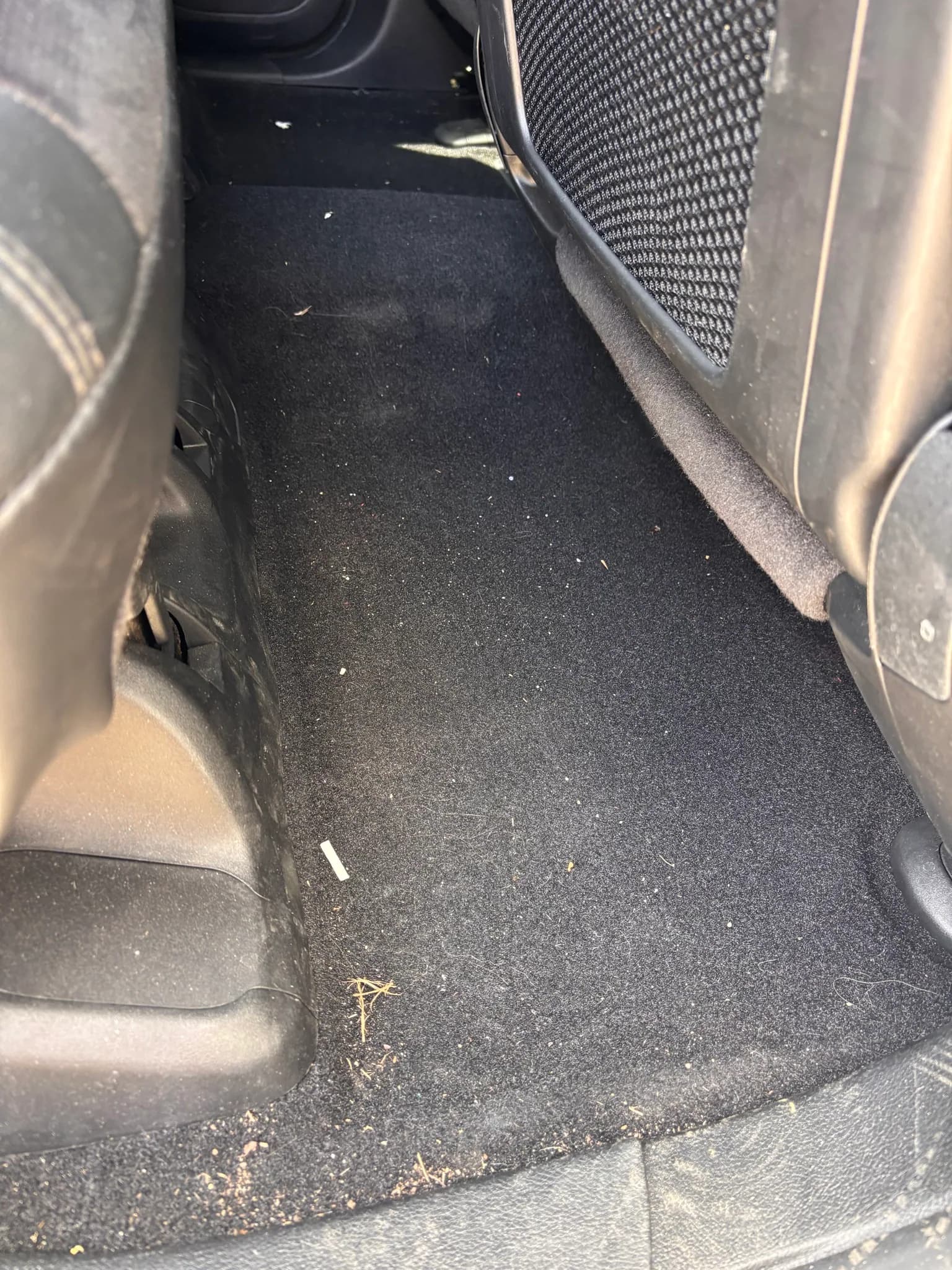 Rear footwell carpet of a Jeep Grand Cherokee with crumbs and debris before cleaning.