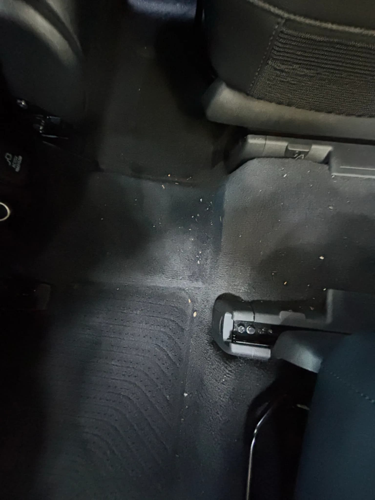 Crumbs scattered on the rear carpet under a seat in a Kia Sorento before cleaning.