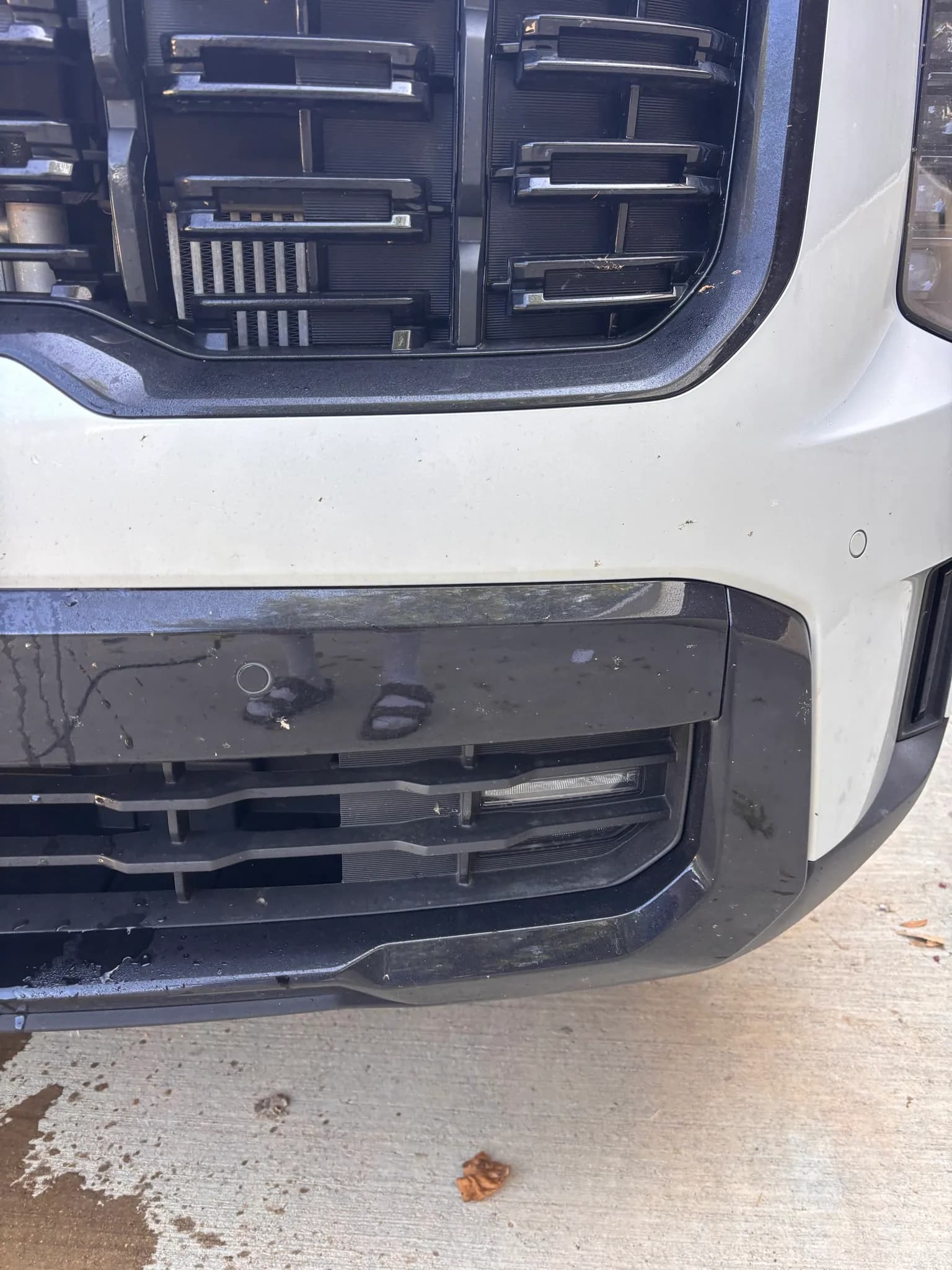 Close-up of a white SUV's lower grille and bumper still dirty with bug splatter and road grime before cleaning.