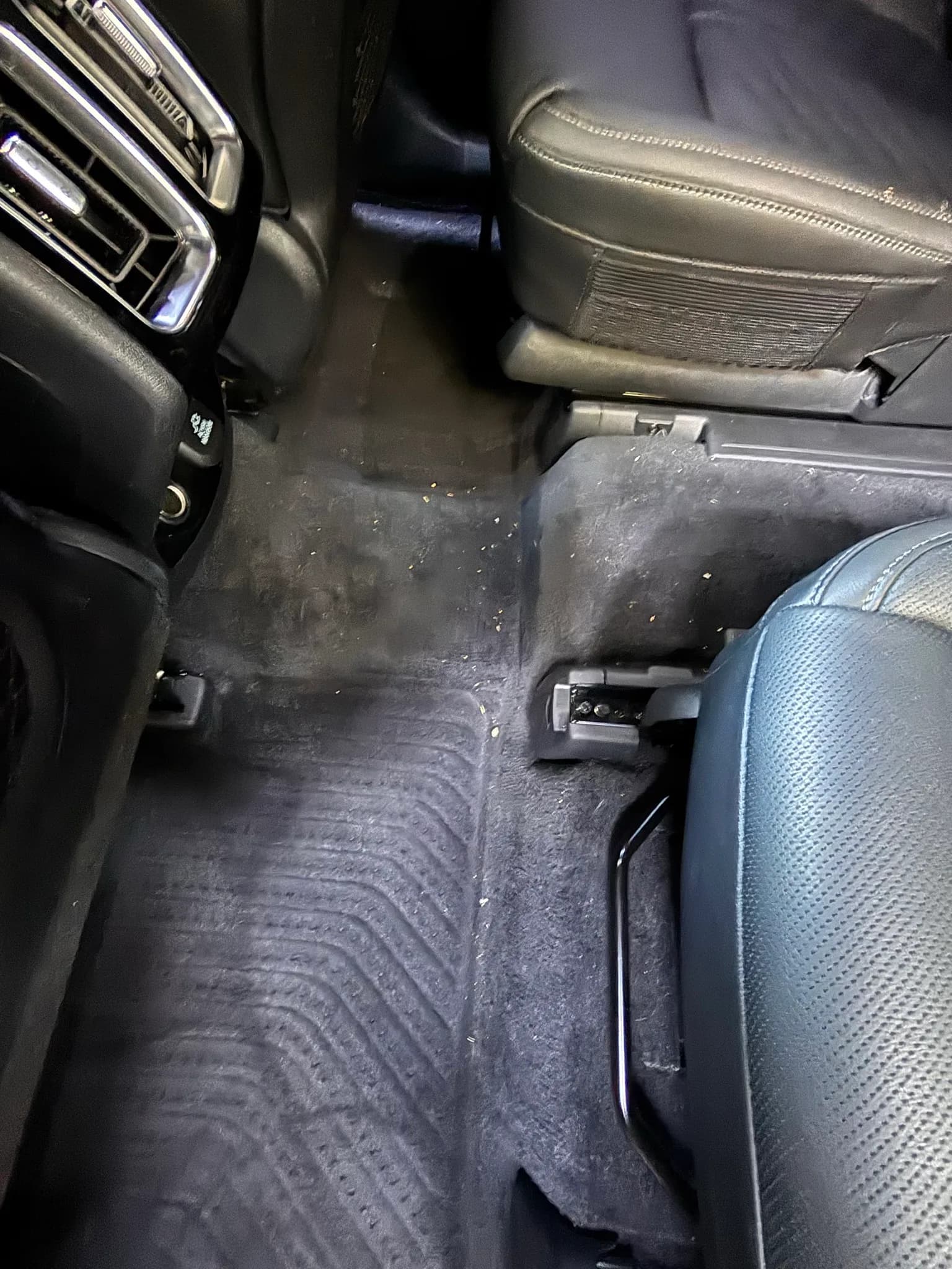 Rear footwell carpet of a Kia Sorento with crumbs and debris before vacuuming.
