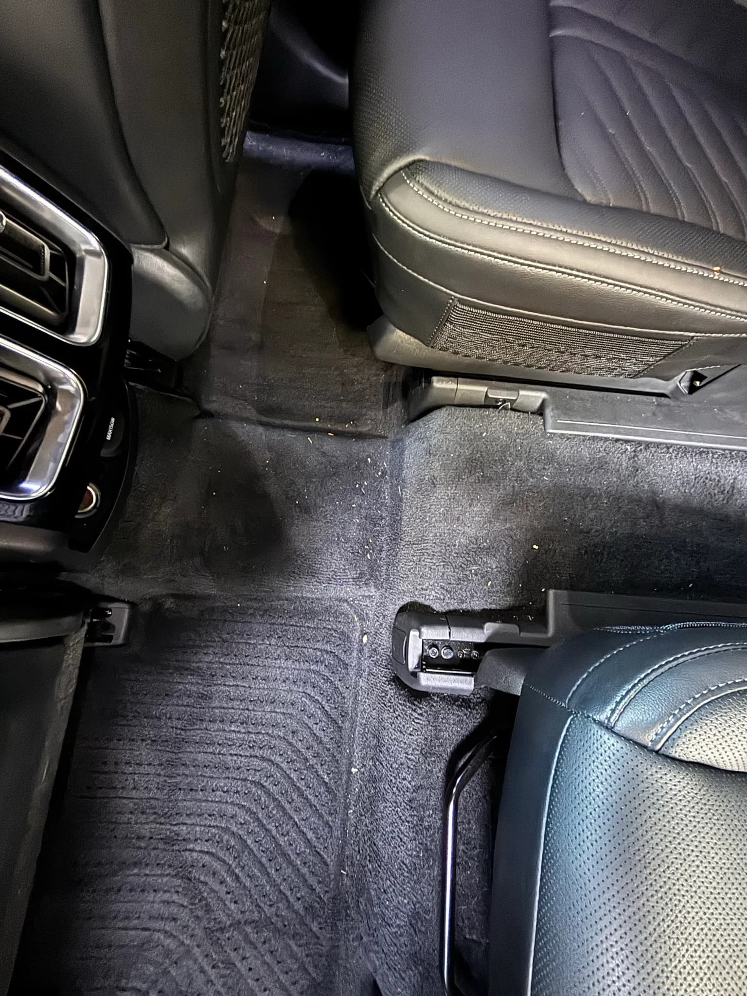 Soiled rear floor carpet and seat rails of a Kia Sorento before interior detailing.