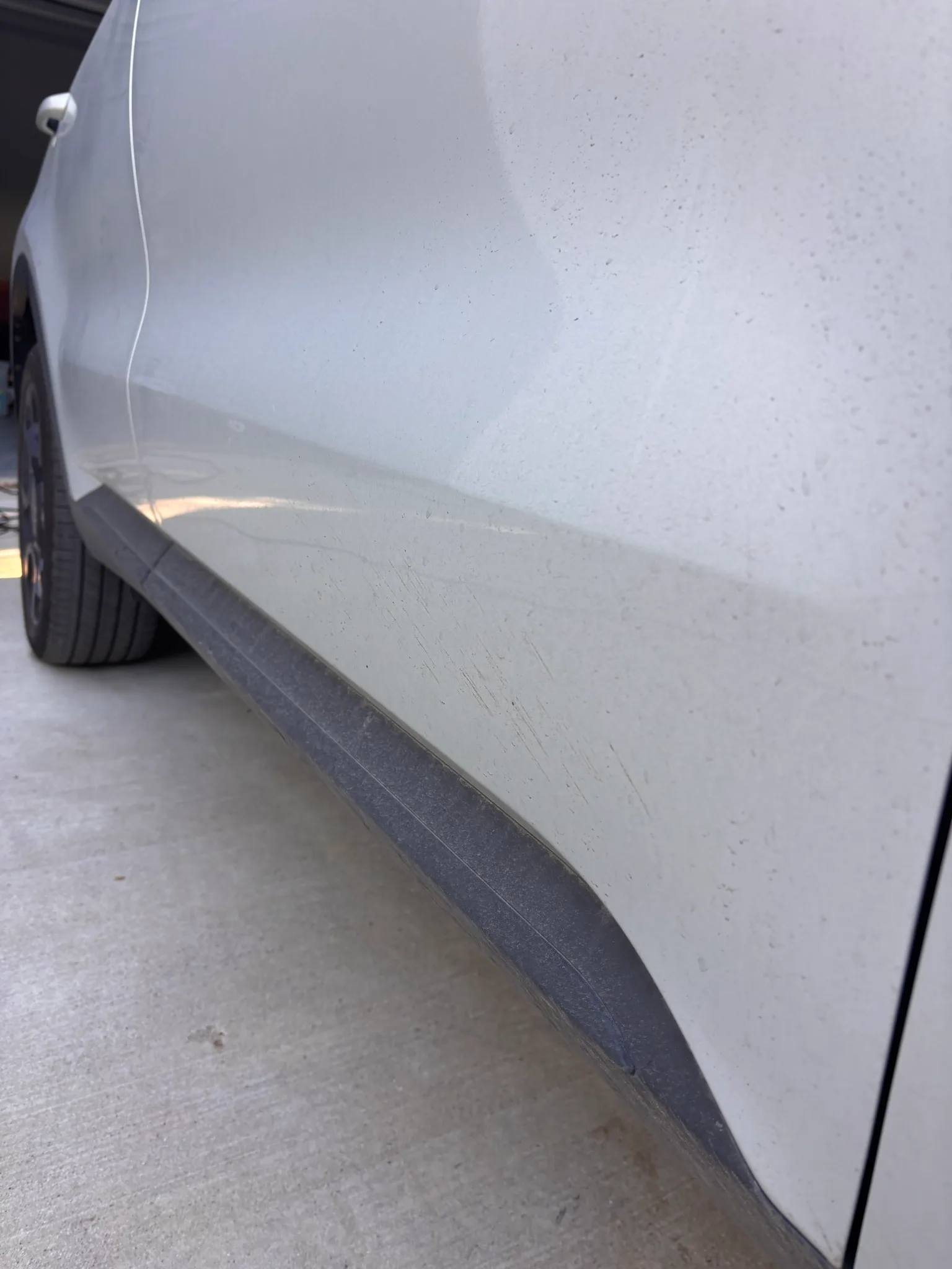 Dirty lower door and rocker panel of a white SUV covered in road grime before washing.