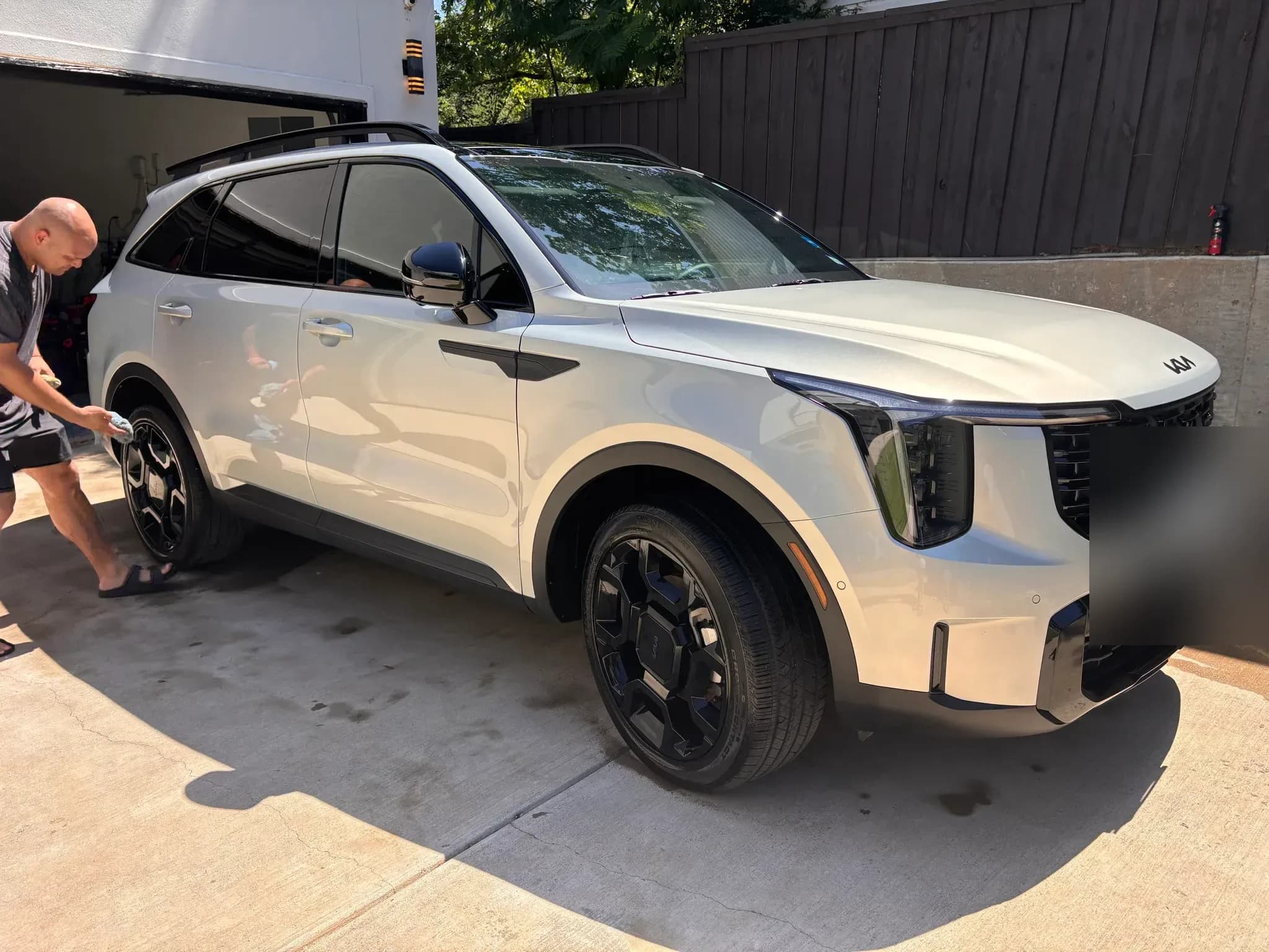 Detailer hand-cleaning the wheel of a white Kia Sorento in a driveway.
