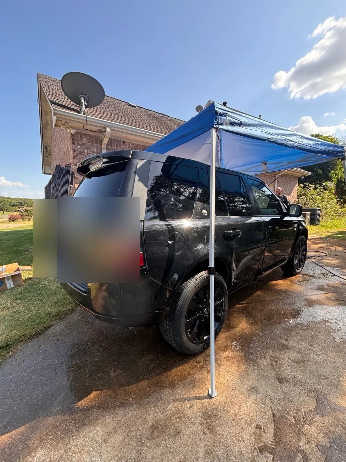 Black Land Rover LR2 parked under a blue pop-up canopy on a wet driveway during a mobile detail.