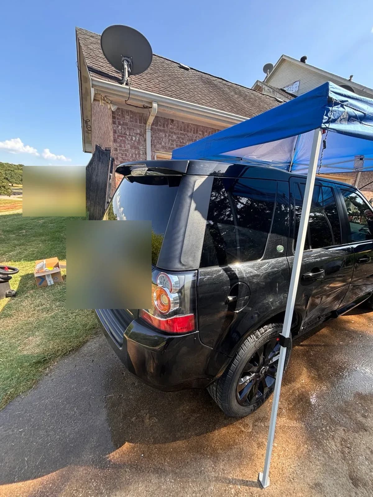 Rear of a black Land Rover LR2 under a portable canopy with detailing equipment on the lawn nearby.