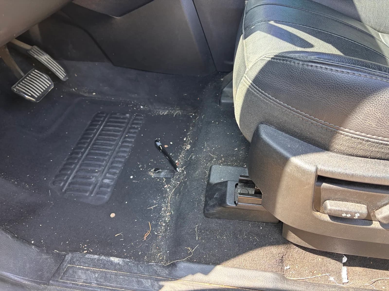 Driver footwell with debris and grass scattered across the carpet before an interior detail.