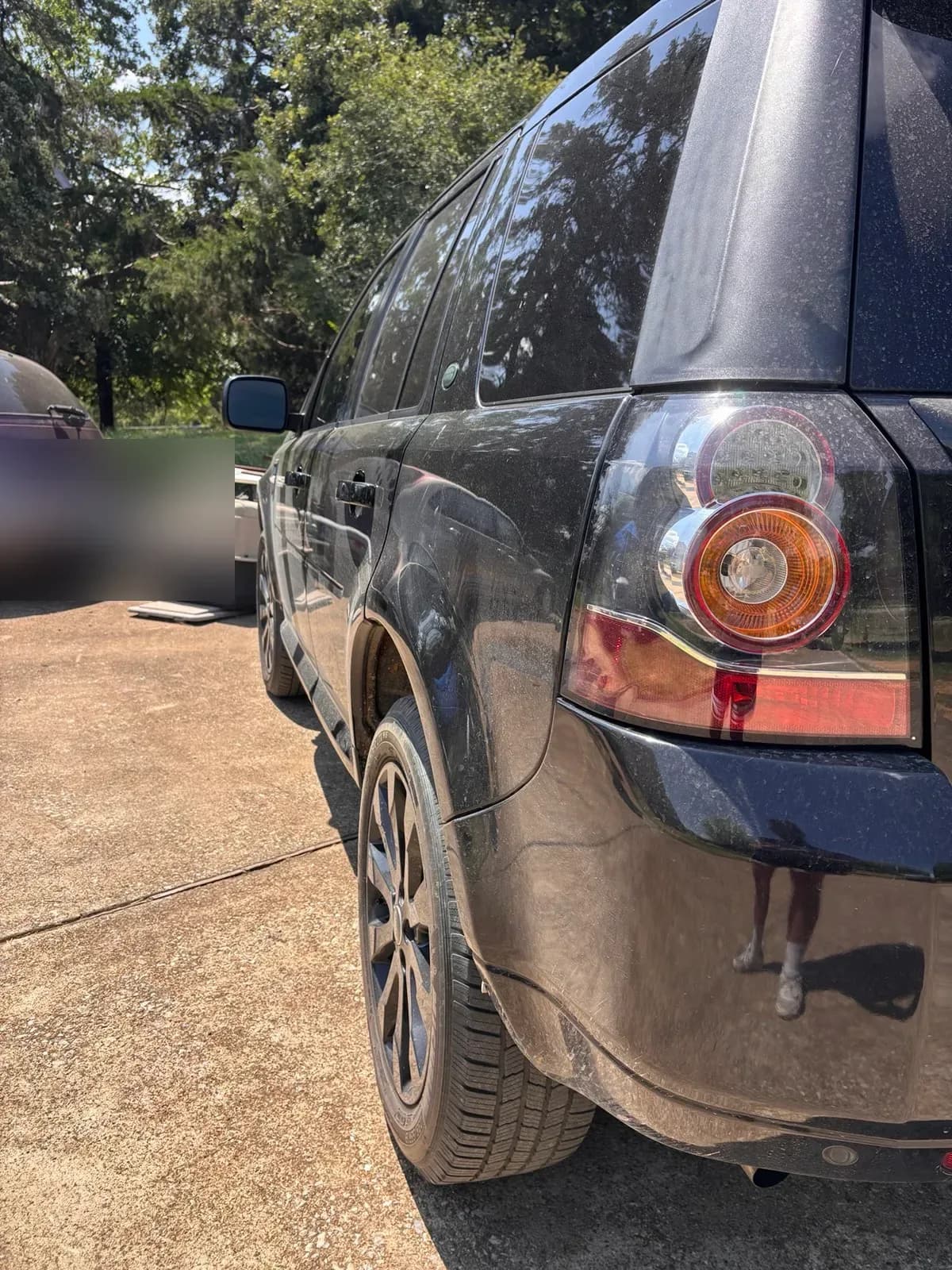 Rear corner of a grimy black Land Rover LR2 showing heavy dust and water spots before a wash.