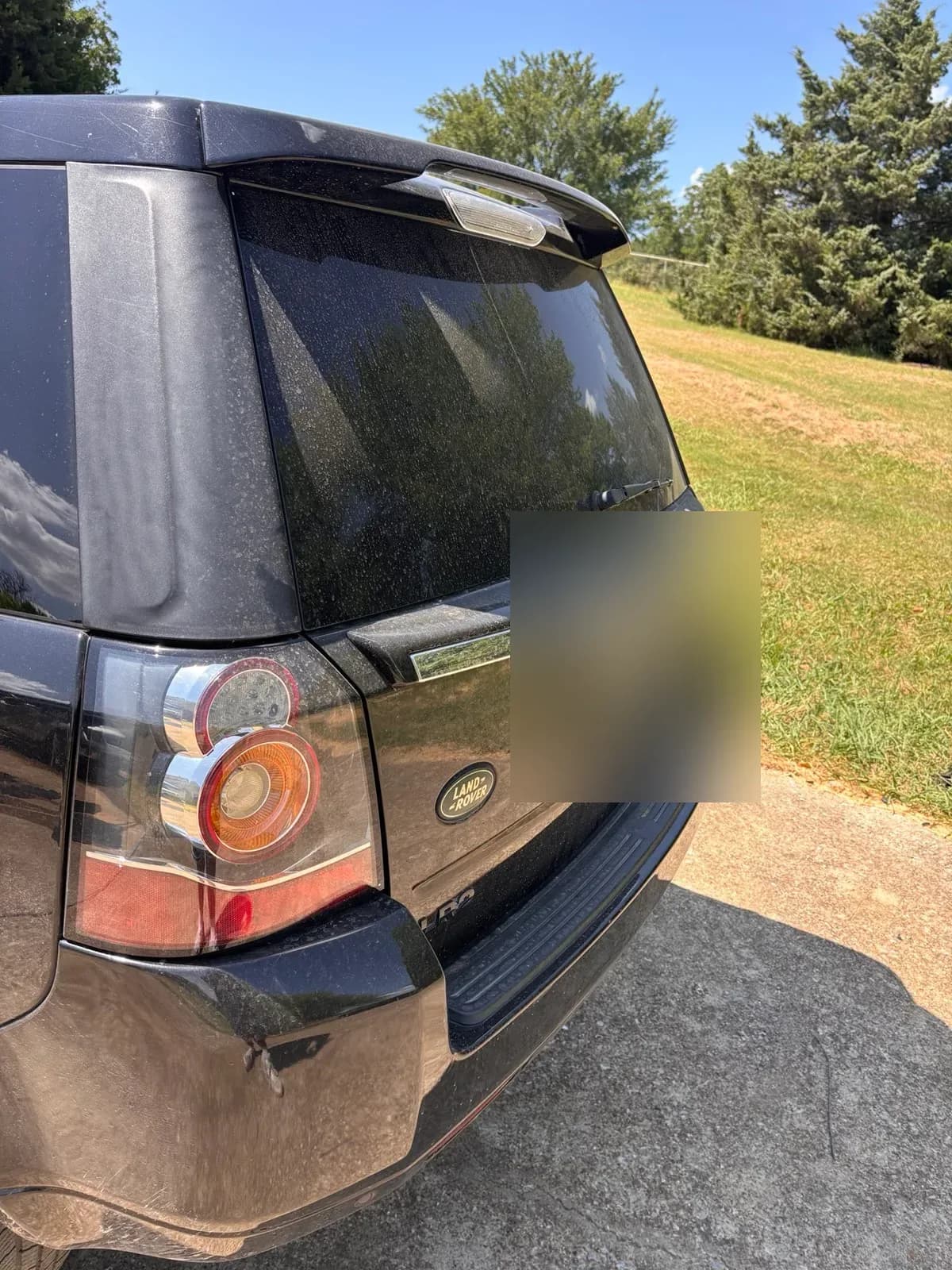 Water-spotted black tailgate and taillight of a Land Rover LR2 before detailing.