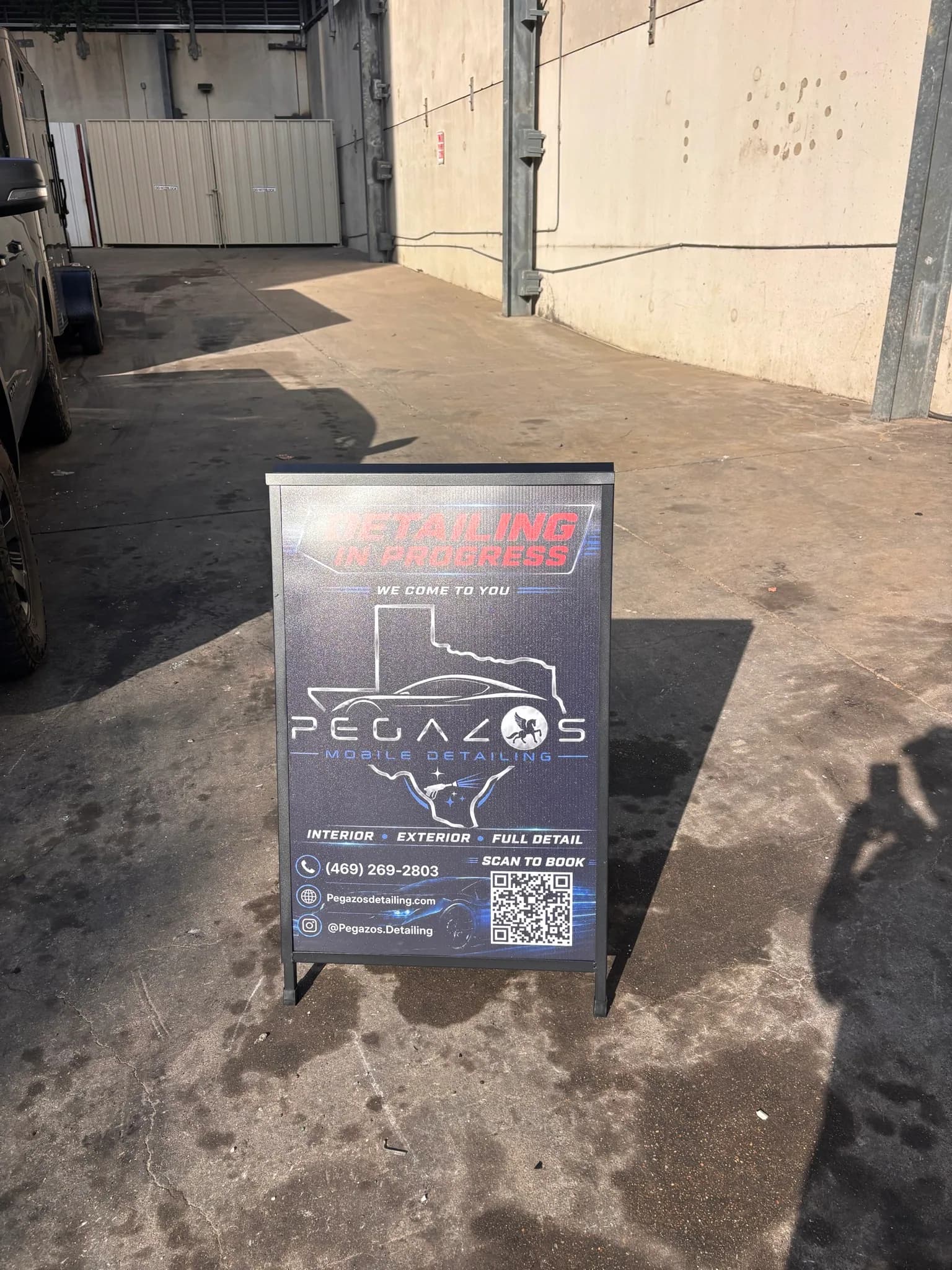 Pegazos Detailing A-frame sign reading detailing in progress at a job site.