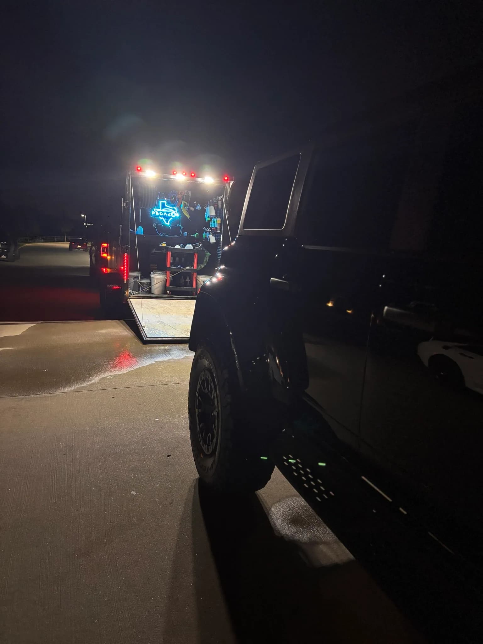The lit detailing trailer working on a black Bronco Raptor after dark.