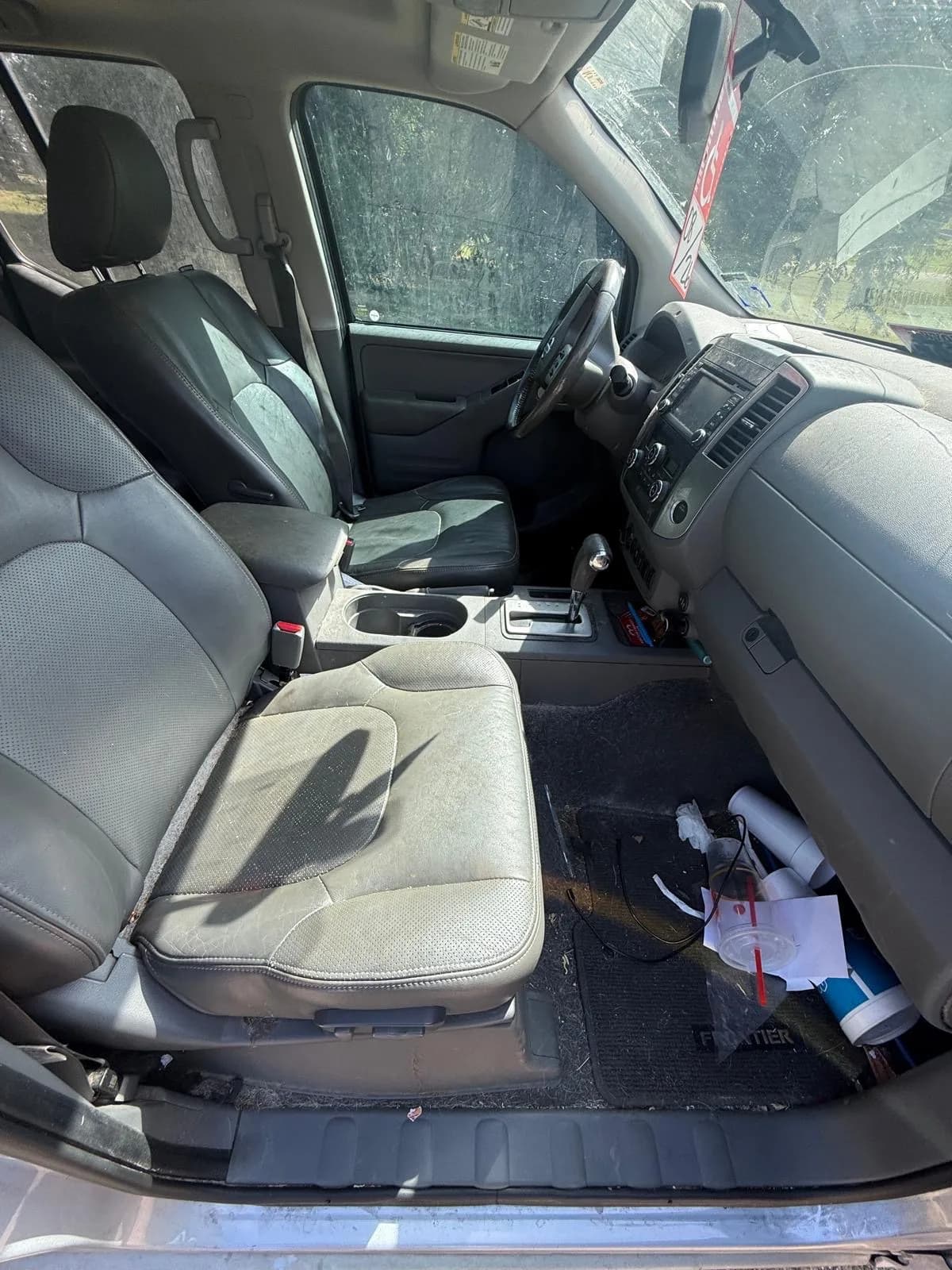 Dirty Nissan Frontier front cabin with stained seats and trash on the passenger floor before an interior detail.