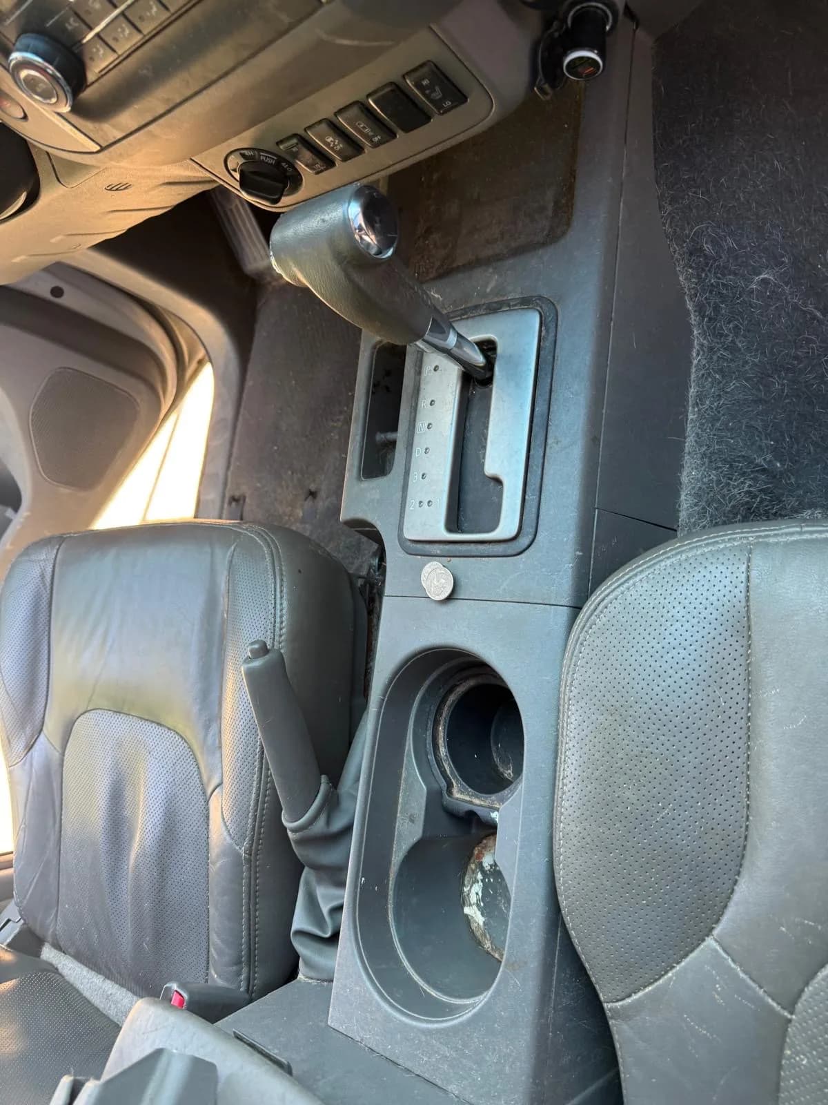 Grimy center console and cup holders between worn leather seats before an interior clean.