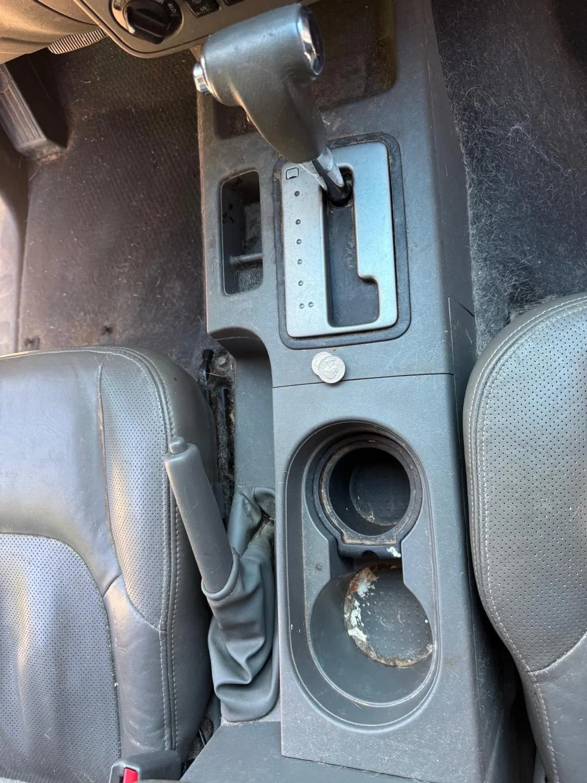 Overhead view of grimy cup holders and console in a truck cabin before cleaning.