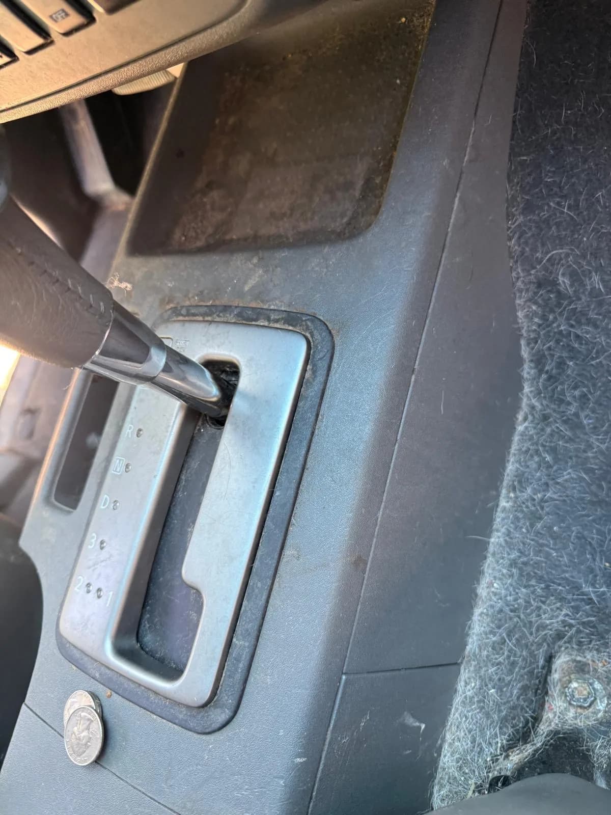 A dirty automatic shifter bezel with a stray coin and dusty console before cleaning.