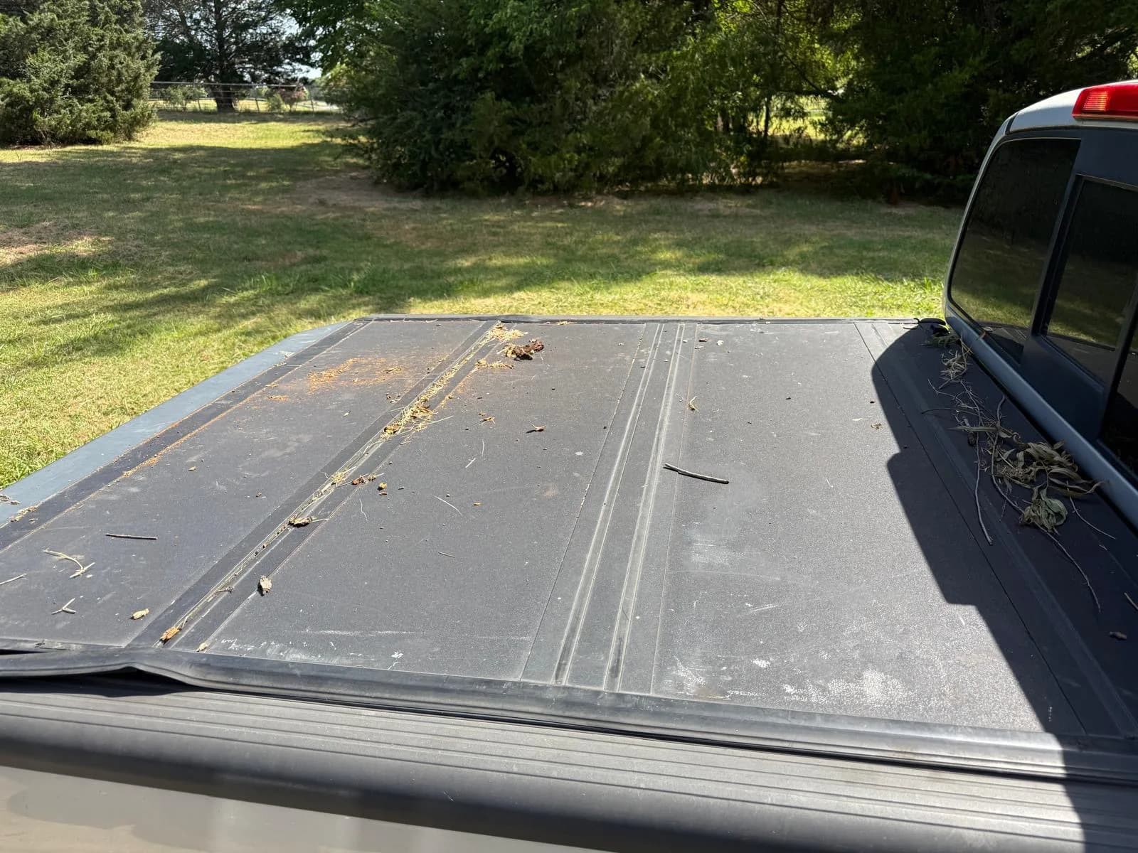A dusty truck bed tonneau cover covered in leaves and debris before cleaning.
