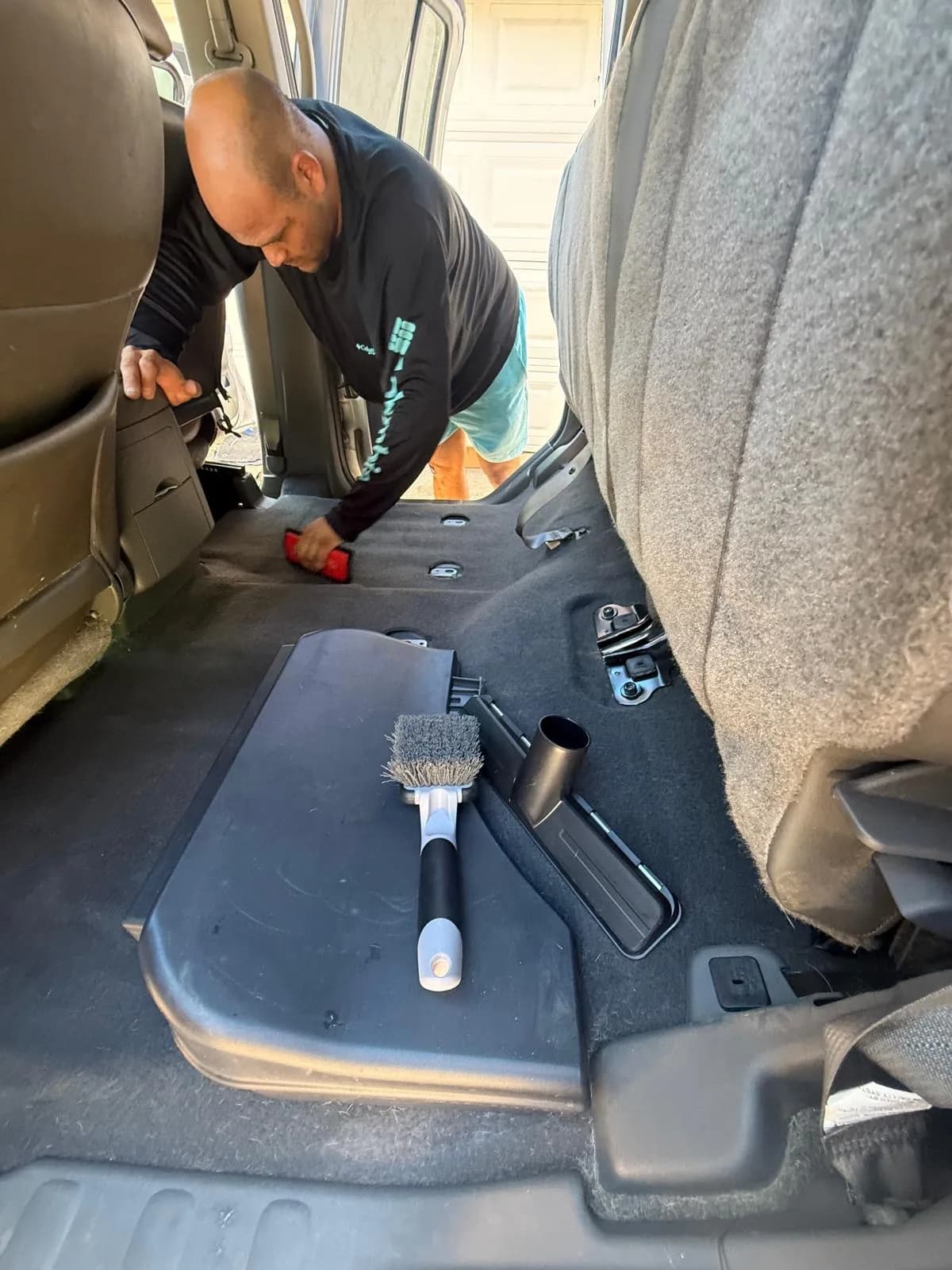 A detailer scrubs the rear floor while a brush and vacuum tools rest on the removed seat base.