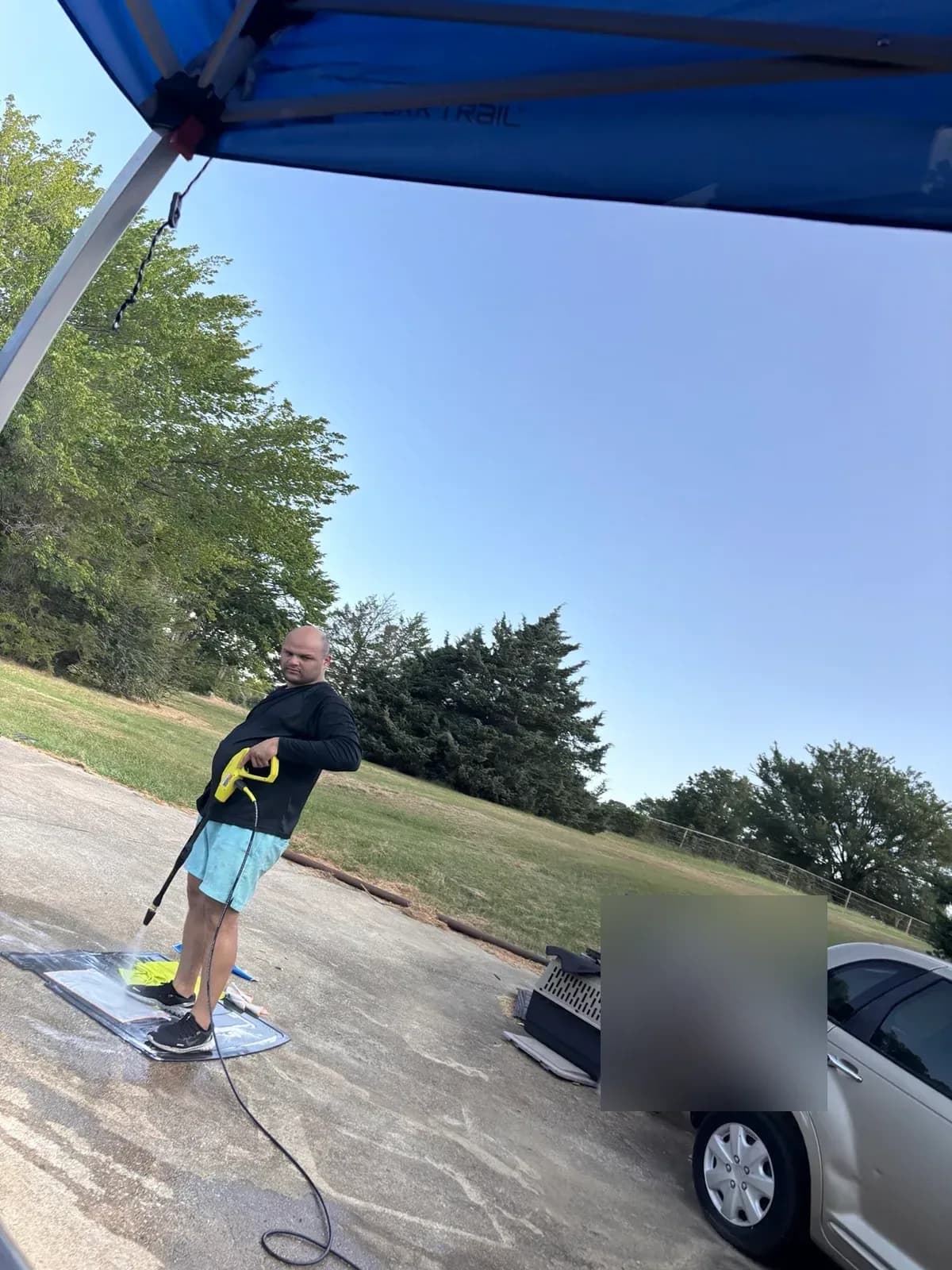 Mobile detailing setup under a pop-up canopy with a detailer pressure washing floor mats.