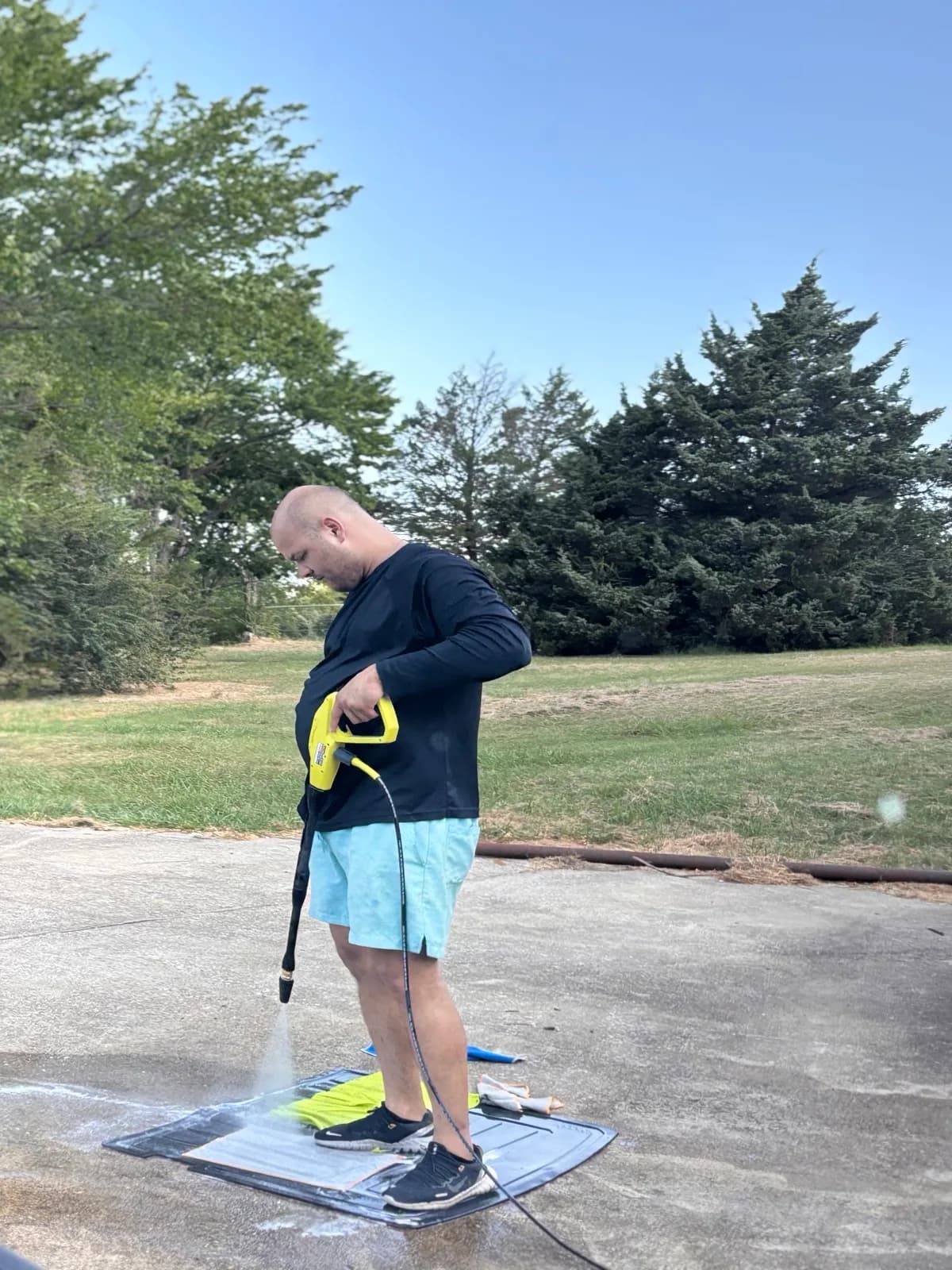 Detailer pressure-rinsing removed floor mats on a driveway.